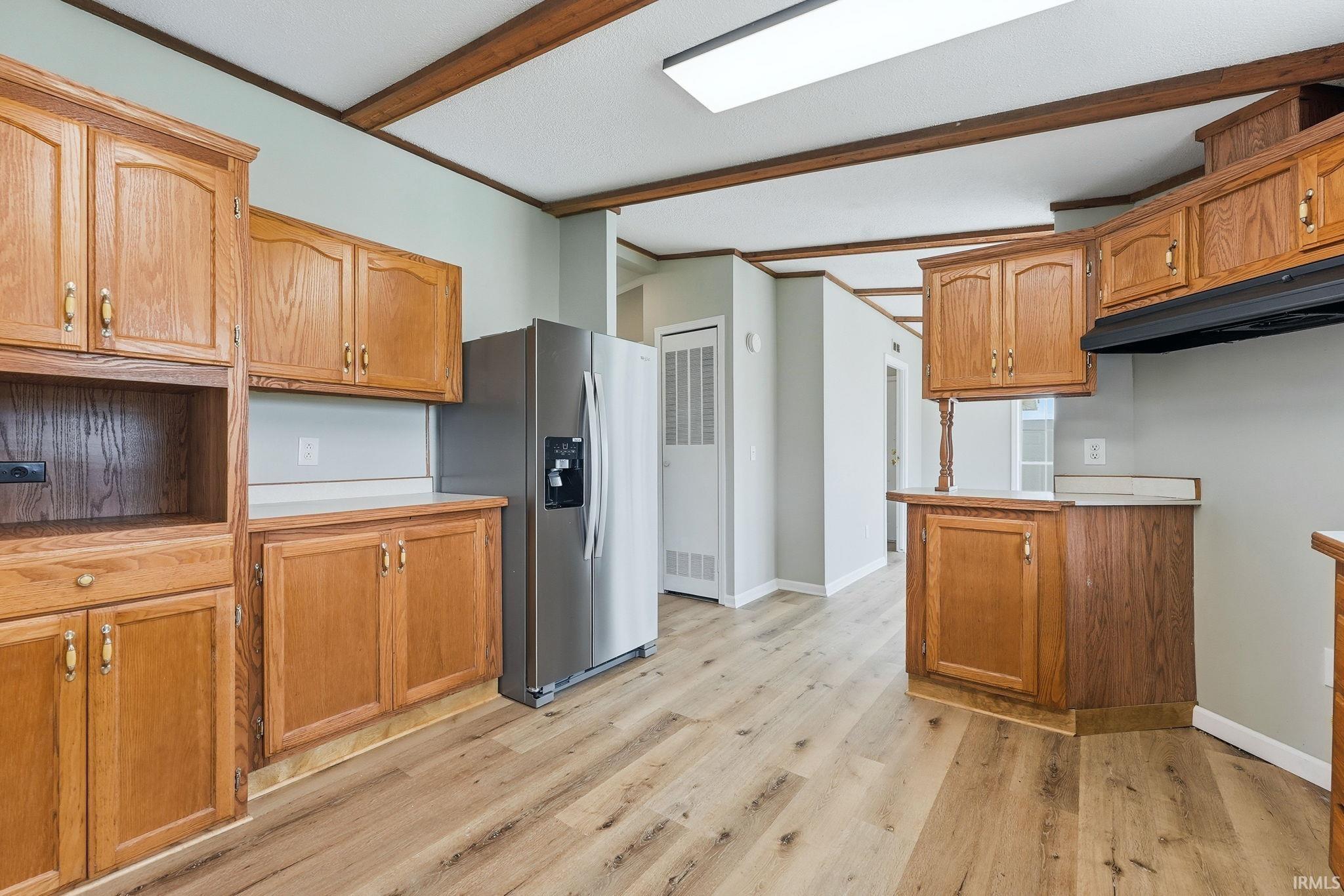 Kitchen featuring wood-finish cabinetry, light countertops, wood-finish flooring, and a stainless steel refrigerator