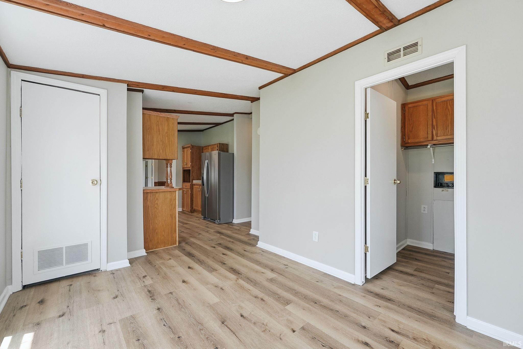 Open concept living area featuring wood-finish flooring, exposed ceiling beams, a neutral color palette, and a dedicated laundry area with built-in cabinetry