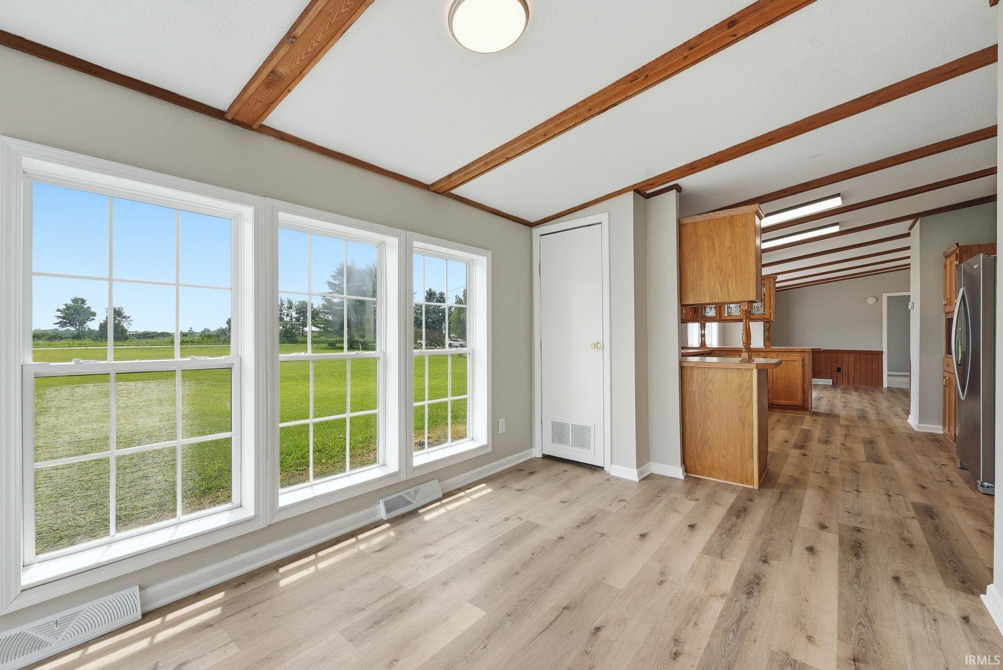 Room with three grid-pattern windows, wood-finish flooring, and exposed wood ceiling beams