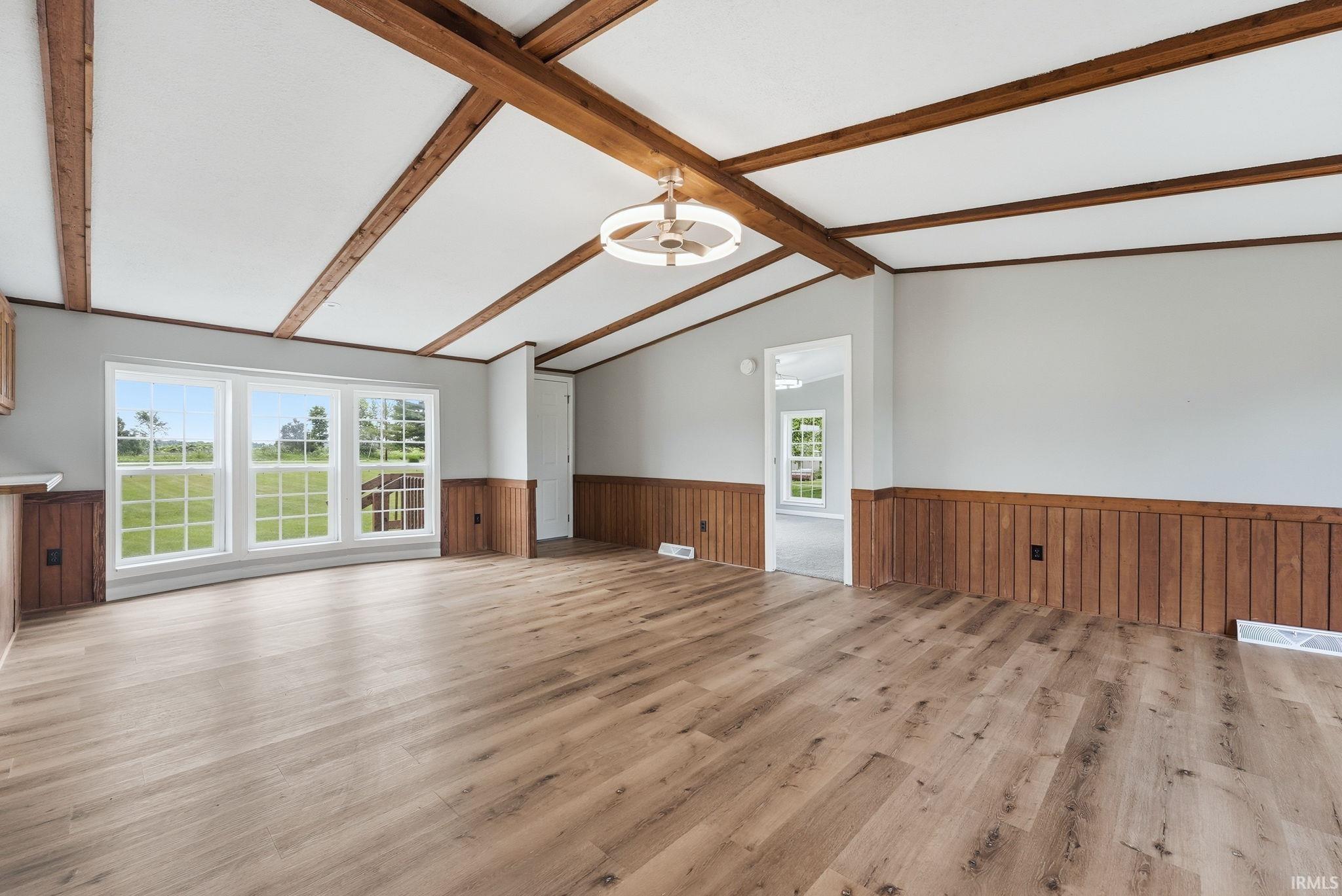 Spacious room with wood-finish flooring, white walls, and a vaulted ceiling featuring exposed wood beams