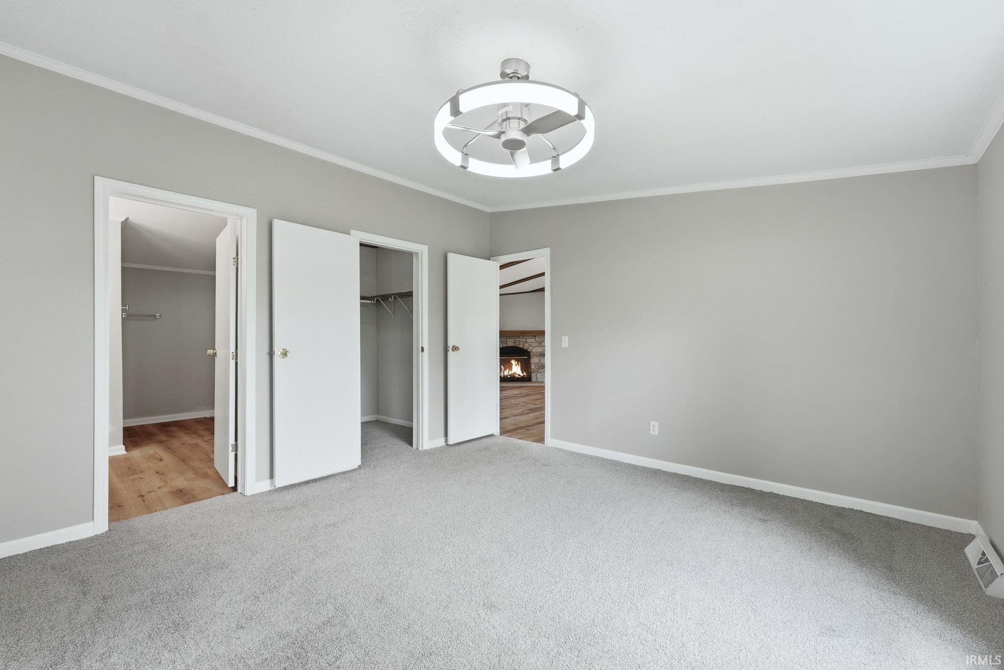 Carpeted room featuring a contemporary ceiling fan with integrated lighting, multiple white interior doors, and a partial glimpse of an additional room with a stone fireplace surround and wood-finish flooring