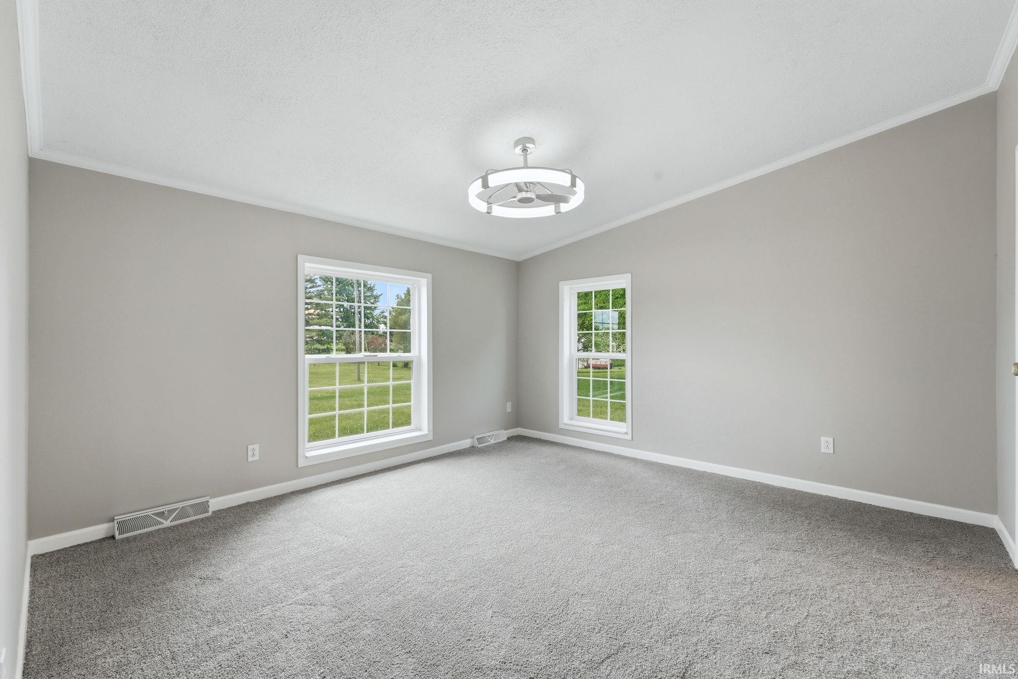 Spacious room with plush gray carpeting, two large windows, white trim, and a contemporary ceiling fan with integrated lighting