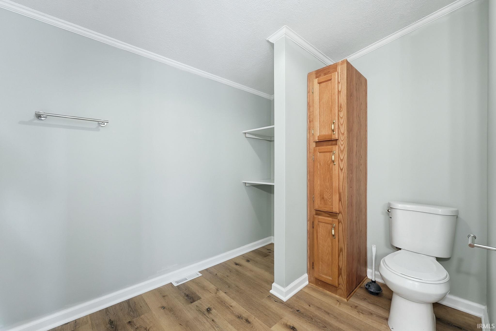 Bathroom featuring wood-finish flooring, a white toilet, and a tall wood-finish storage cabinet