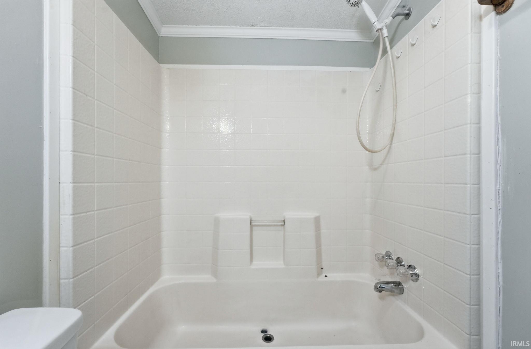 Bathtub and shower combination featuring a white tiled surround, chrome fixtures, and a handheld shower head