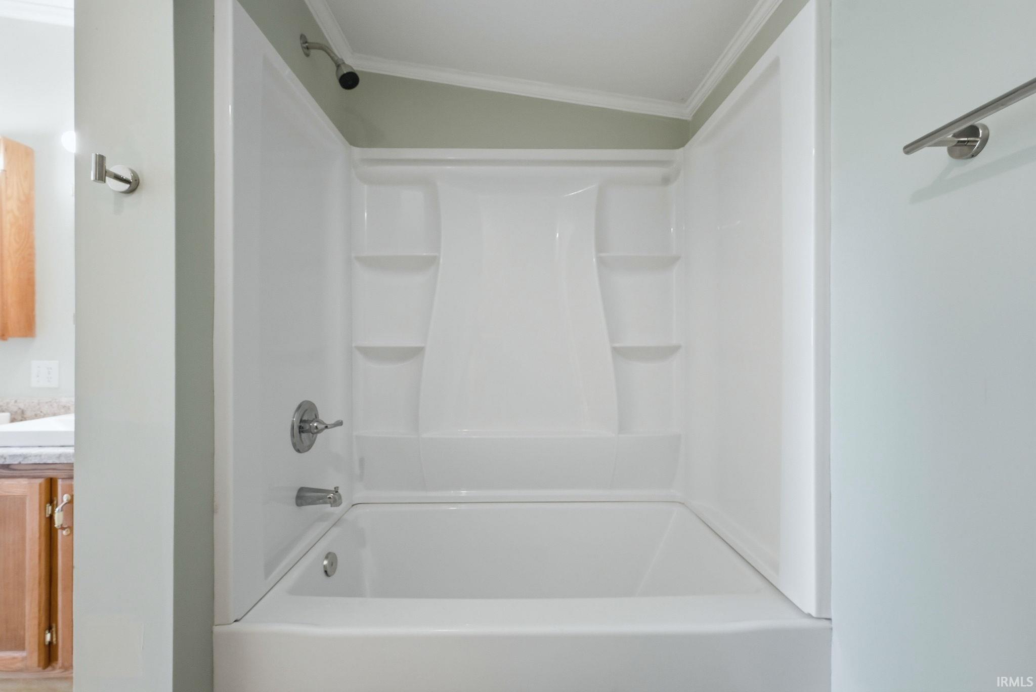 White bathtub and shower combination unit featuring integrated shelving