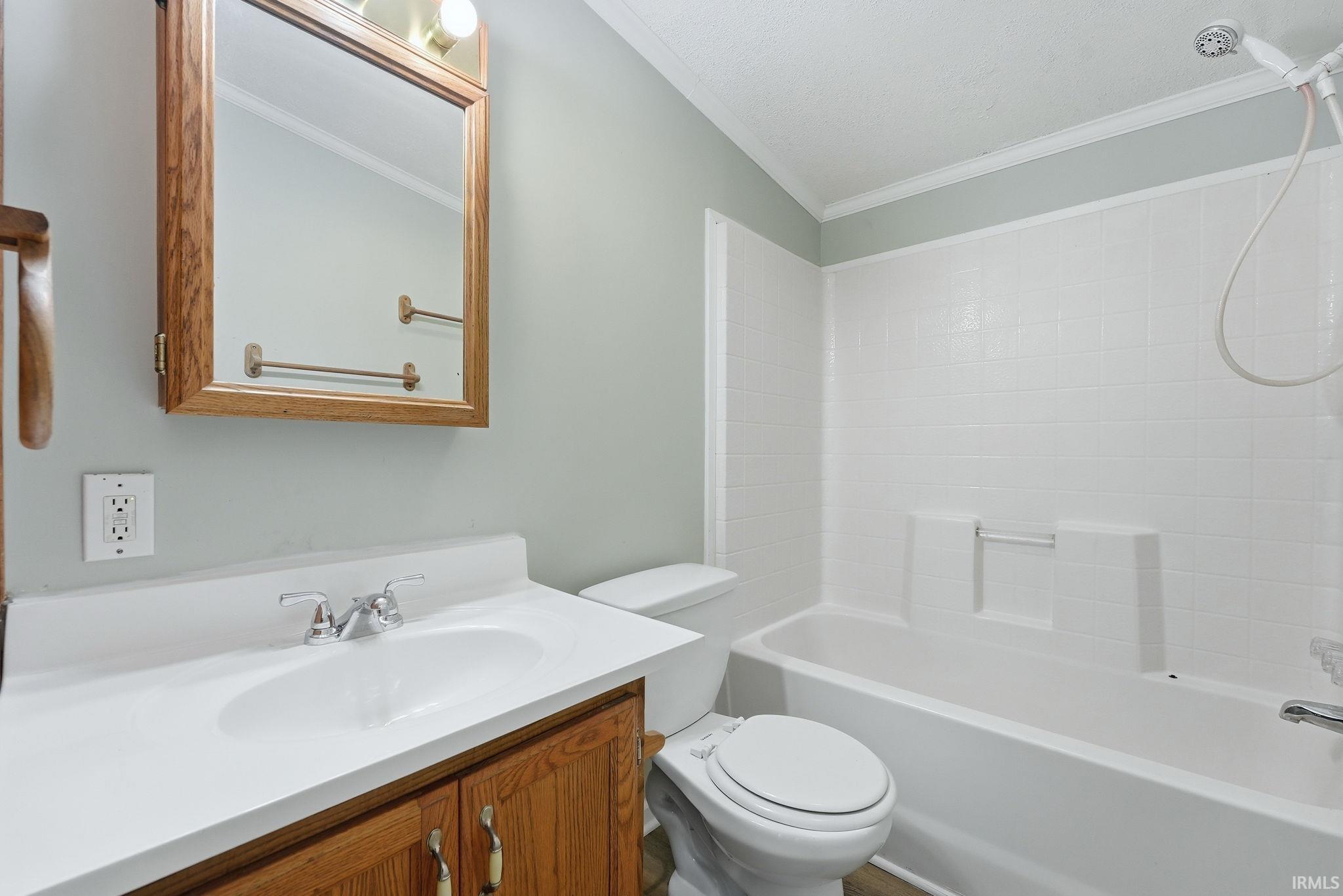 Bathroom featuring a wood-finish vanity with an integrated white sink, a coordinating wood-finish medicine cabinet, chrome faucet hardware, and a white tile shower surround with a built-in tub