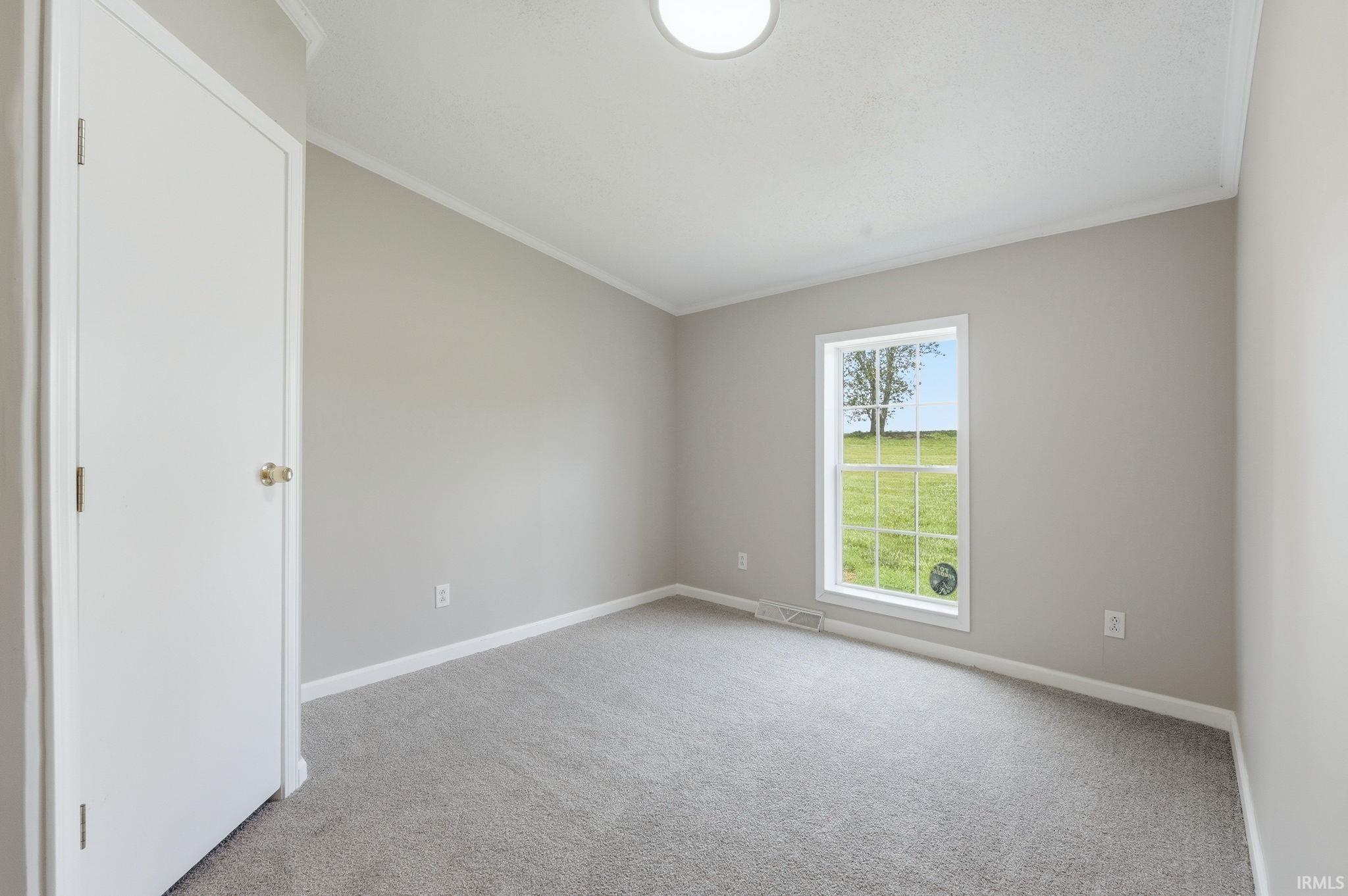 Neutral-toned room featuring a single window with grid panes, plush grey carpeting, and white baseboards