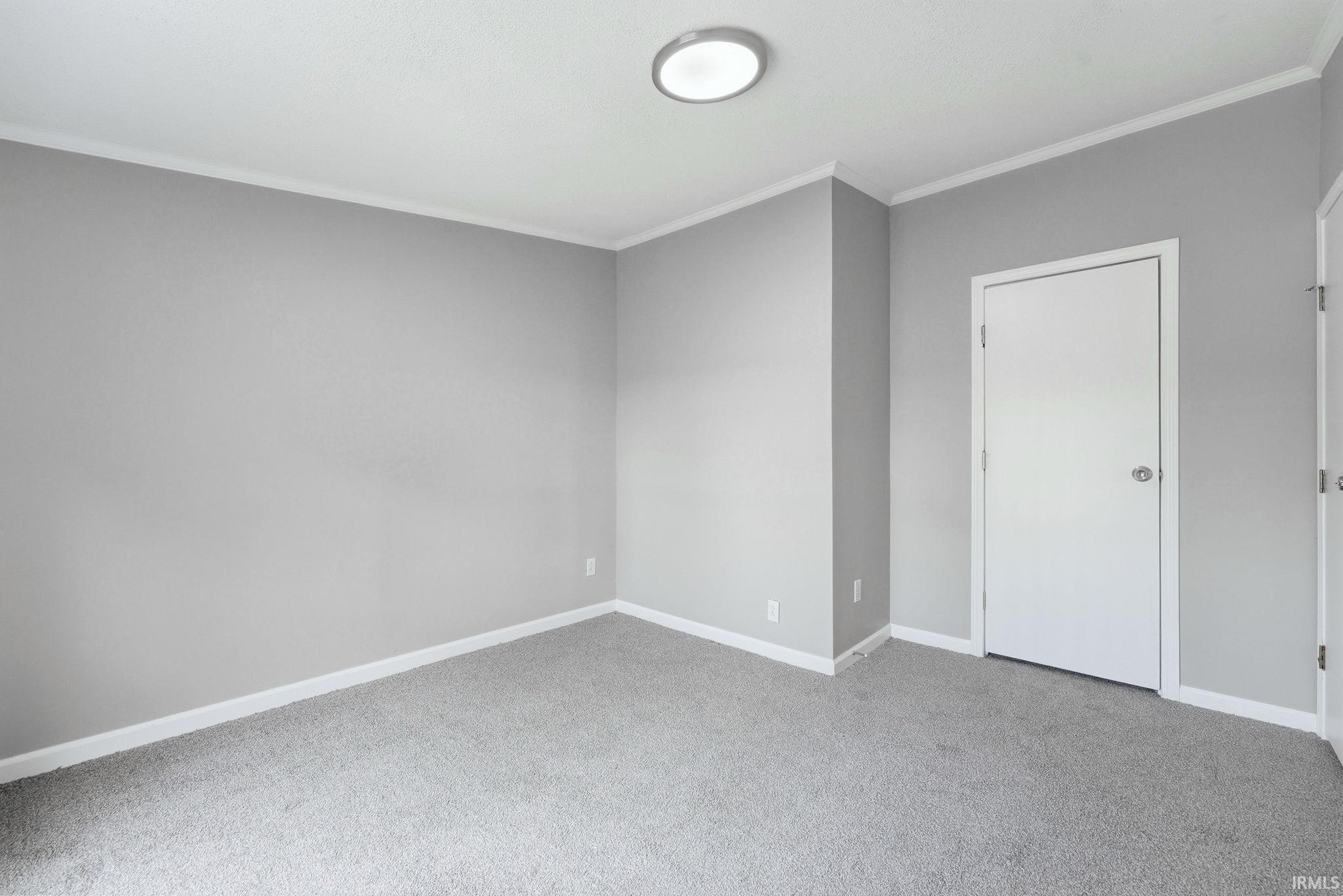 Room featuring light gray wall paint, gray carpet flooring, white baseboards, and white crown molding