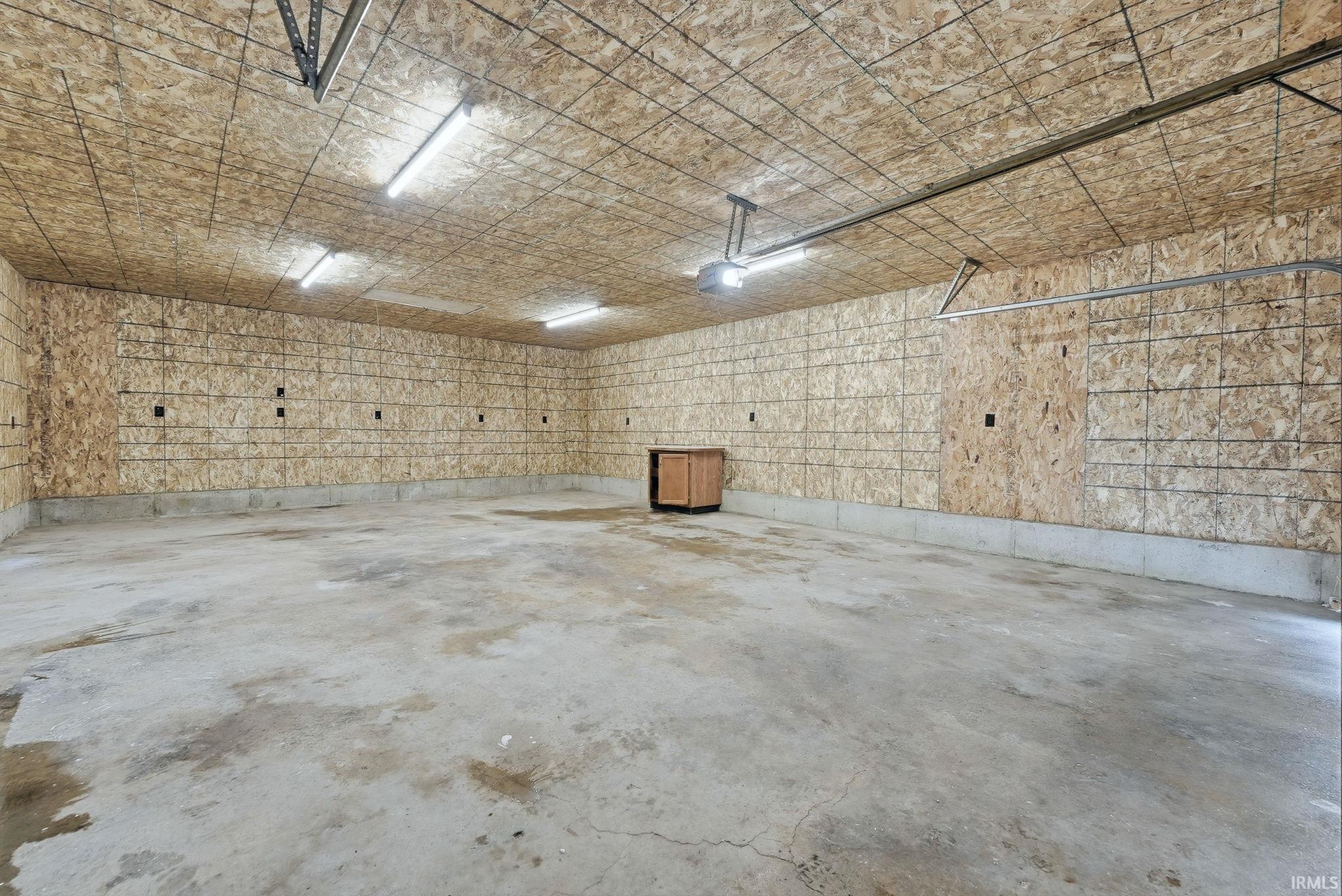 Spacious garage featuring concrete flooring, structural wood paneling, and multiple overhead fluorescent light fixtures