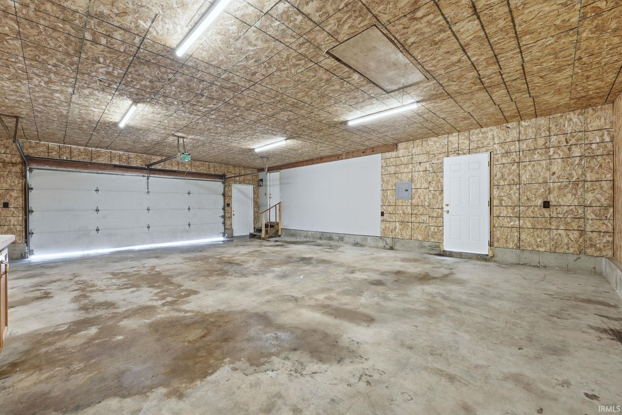 Spacious garage with exposed OSB walls and ceiling, concrete flooring, and multiple overhead fluorescent light fixtures