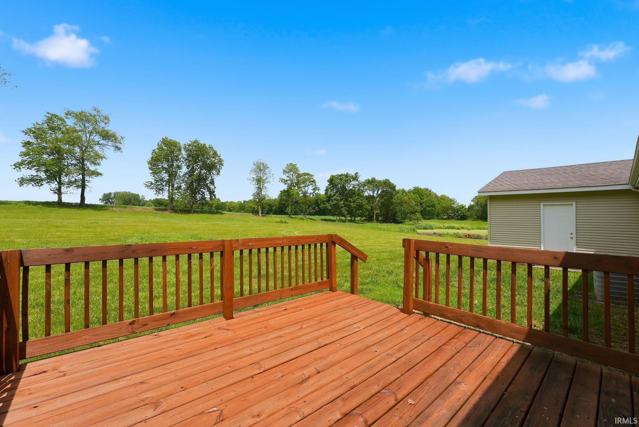 Spacious wooden deck featuring a natural wood finish and sturdy railing, overlooking an expansive green field