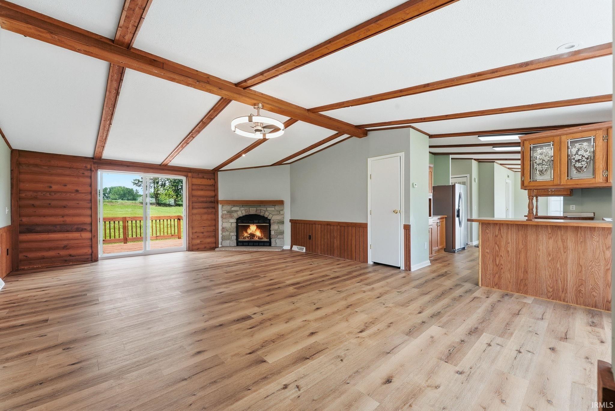 Vaulted ceilings with exposed wood beams highlight this spacious room, featuring wood-finish flooring and a stone fireplace