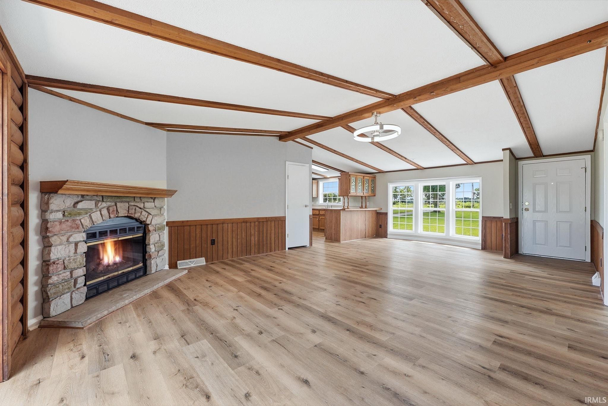 Spacious room featuring a stone-faced fireplace with a wood mantel, wood-finish flooring, and white walls with wood wainscoting