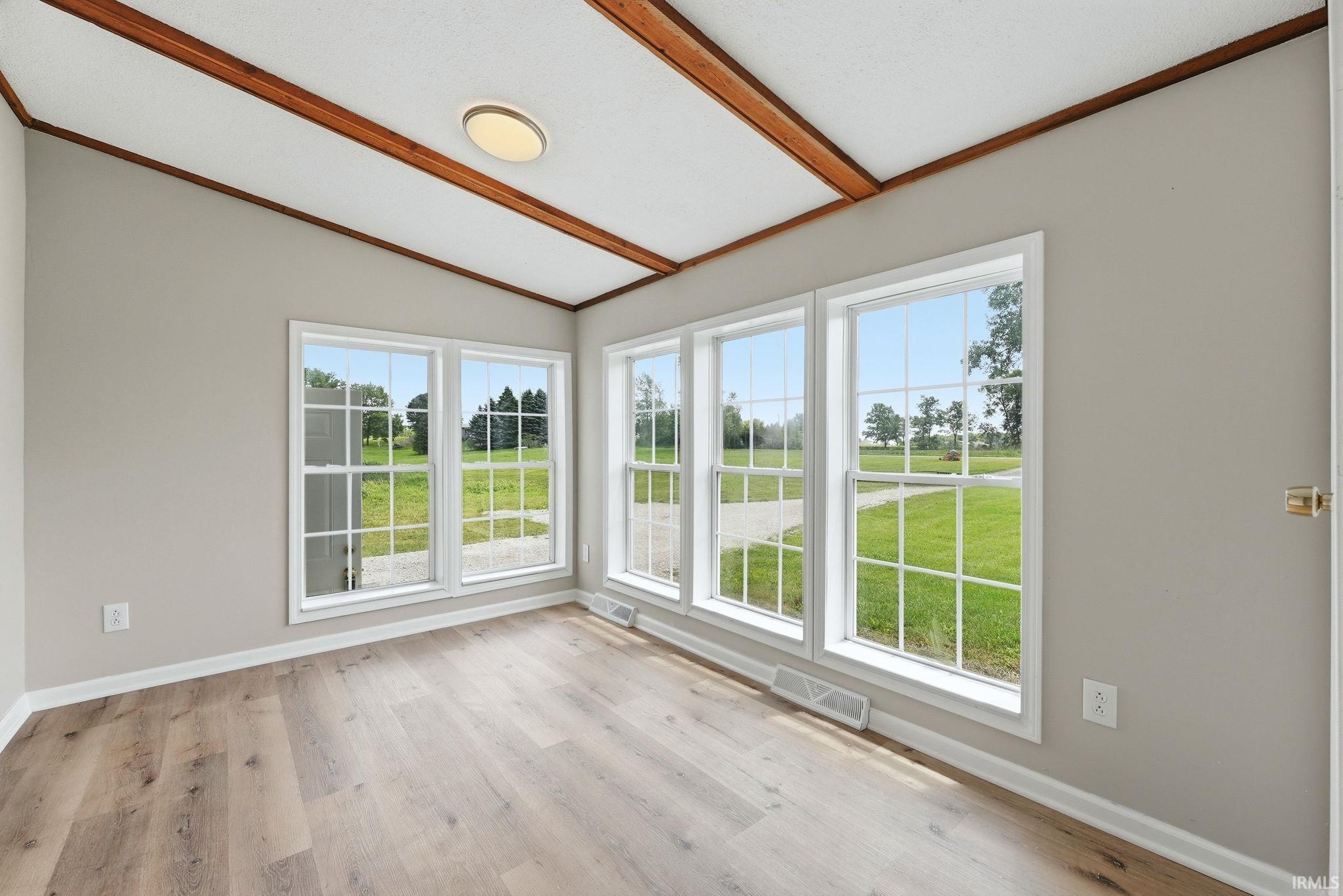 Room featuring abundant natural light, wood-finish flooring, light gray wall paint, white trim, and a white ceiling with exposed wood beams