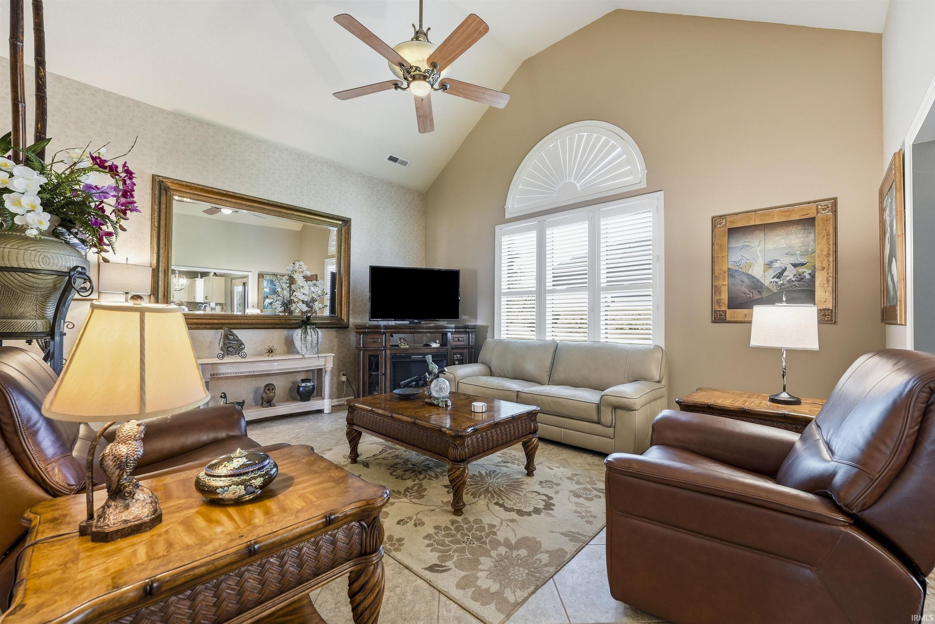 Vaulted ceiling living space with a ceiling fan, arched transom window, and plantation shutters