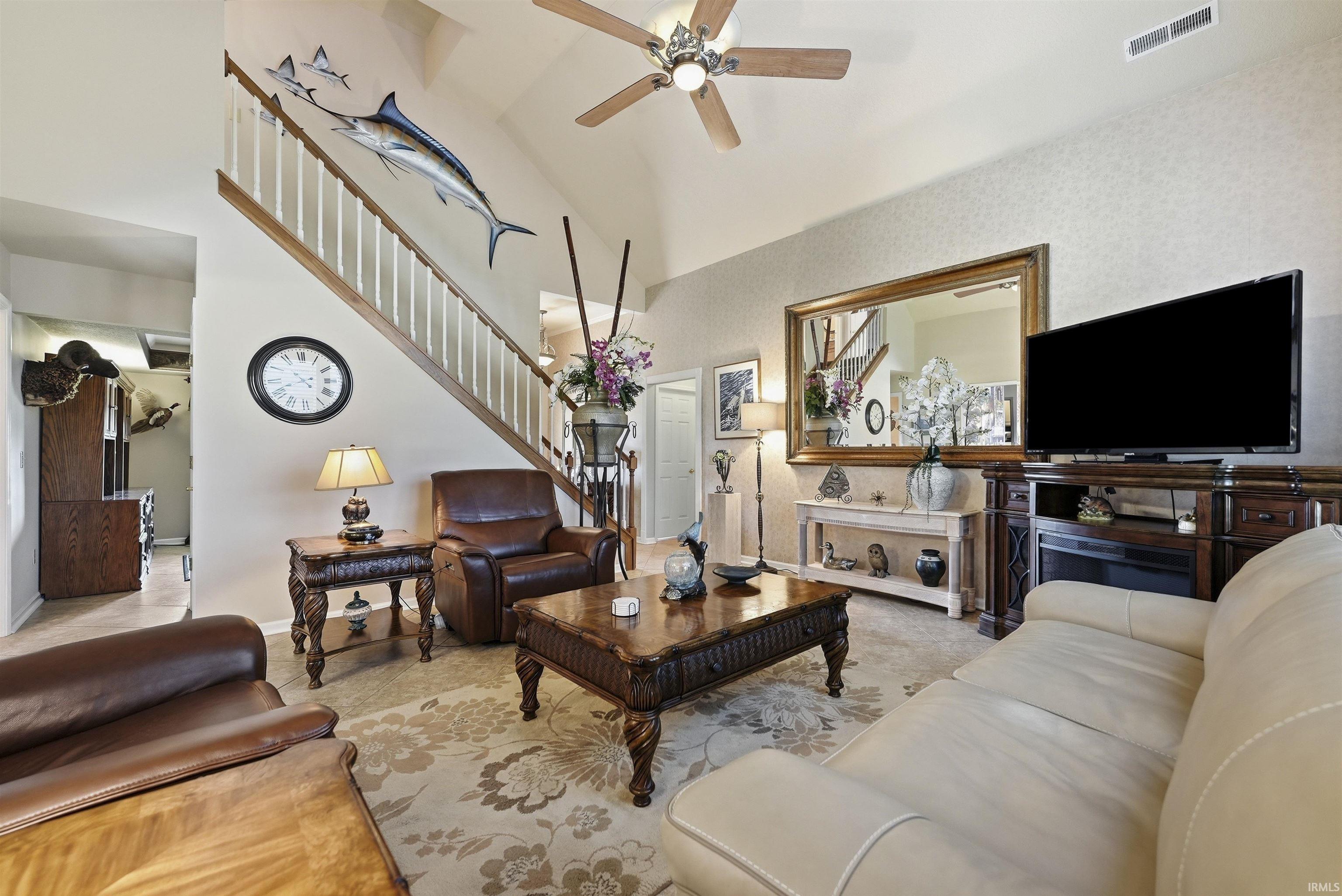 Living area featuring a vaulted ceiling with a ceiling fan, a prominent staircase with white balusters and wood handrails, and an entertainment center with an integrated electric fireplace