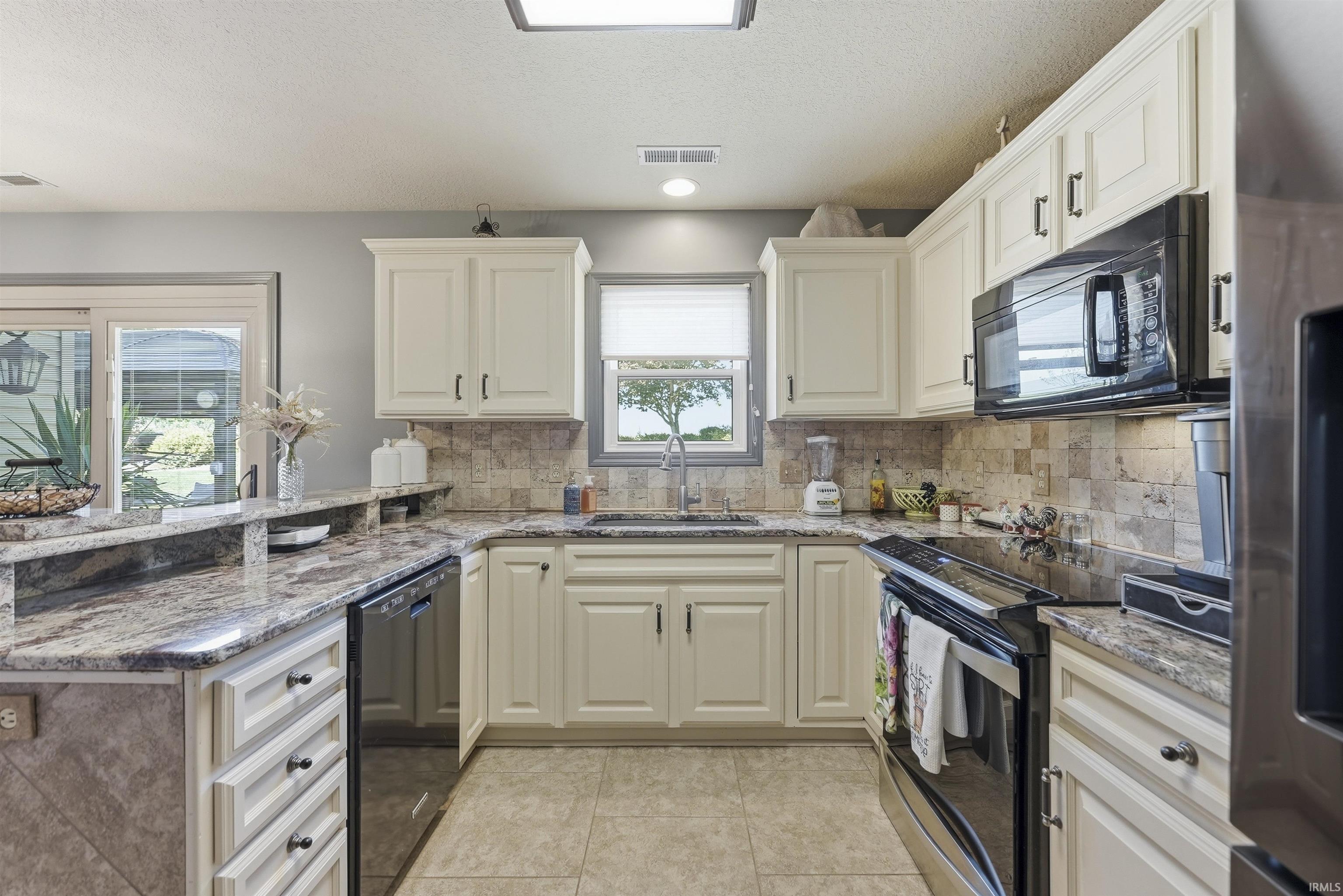 Chef's kitchen featuring cream-colored cabinetry with brushed nickel hardware, granite countertops, subway tile backsplash, and stainless steel appliances including a double wall oven, gas cooktop, and built-in microwave