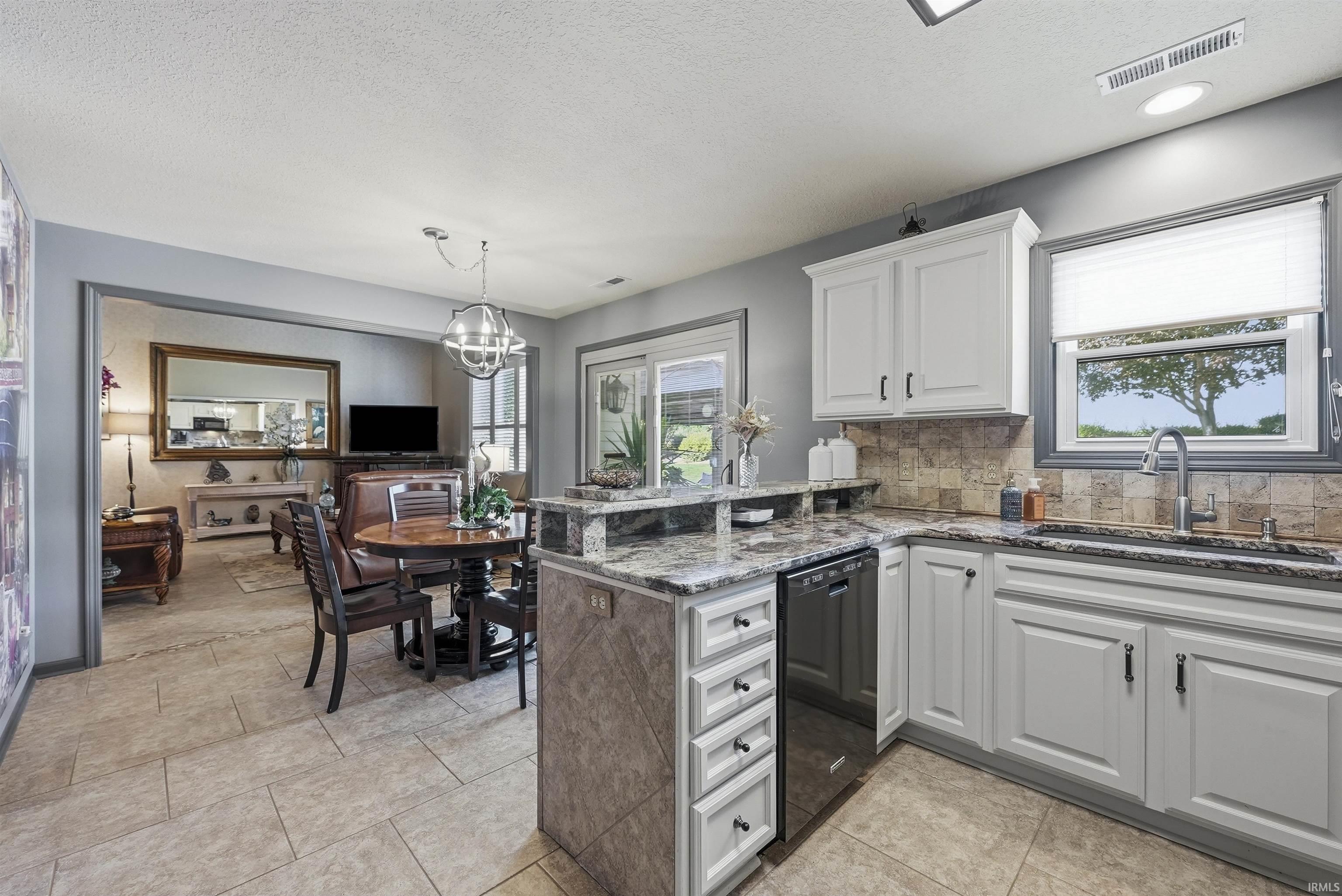 Gourmet kitchen featuring white cabinetry, a gray-and-white marble-finish island with seated dining space, stainless steel appliances, neutral tile flooring, and a subway tile backsplash
