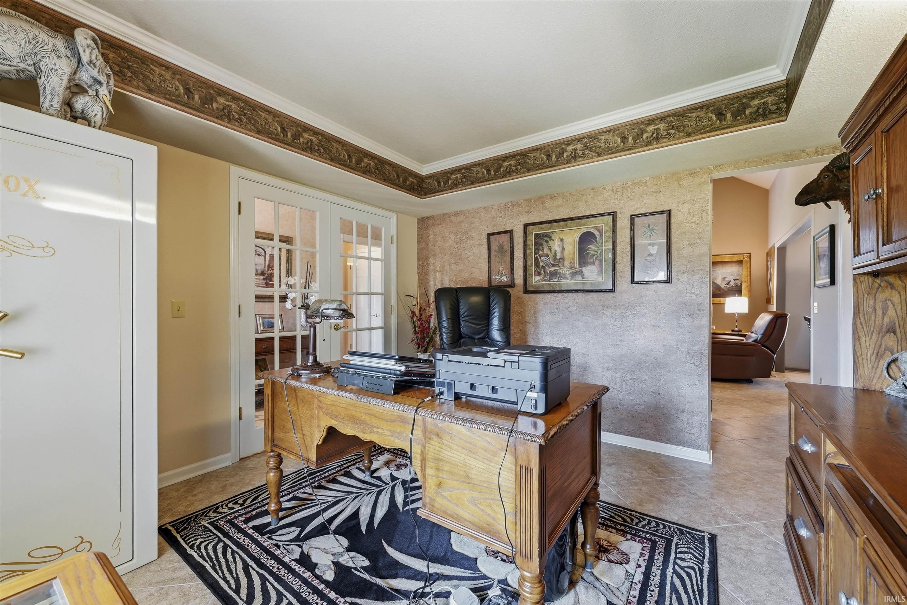 Elegant home office featuring rich wood cabinetry, a substantial wood desk with ample work surface, decorative geometric area rugs in contrasting patterns, and coffered ceiling detail with decorative crown molding