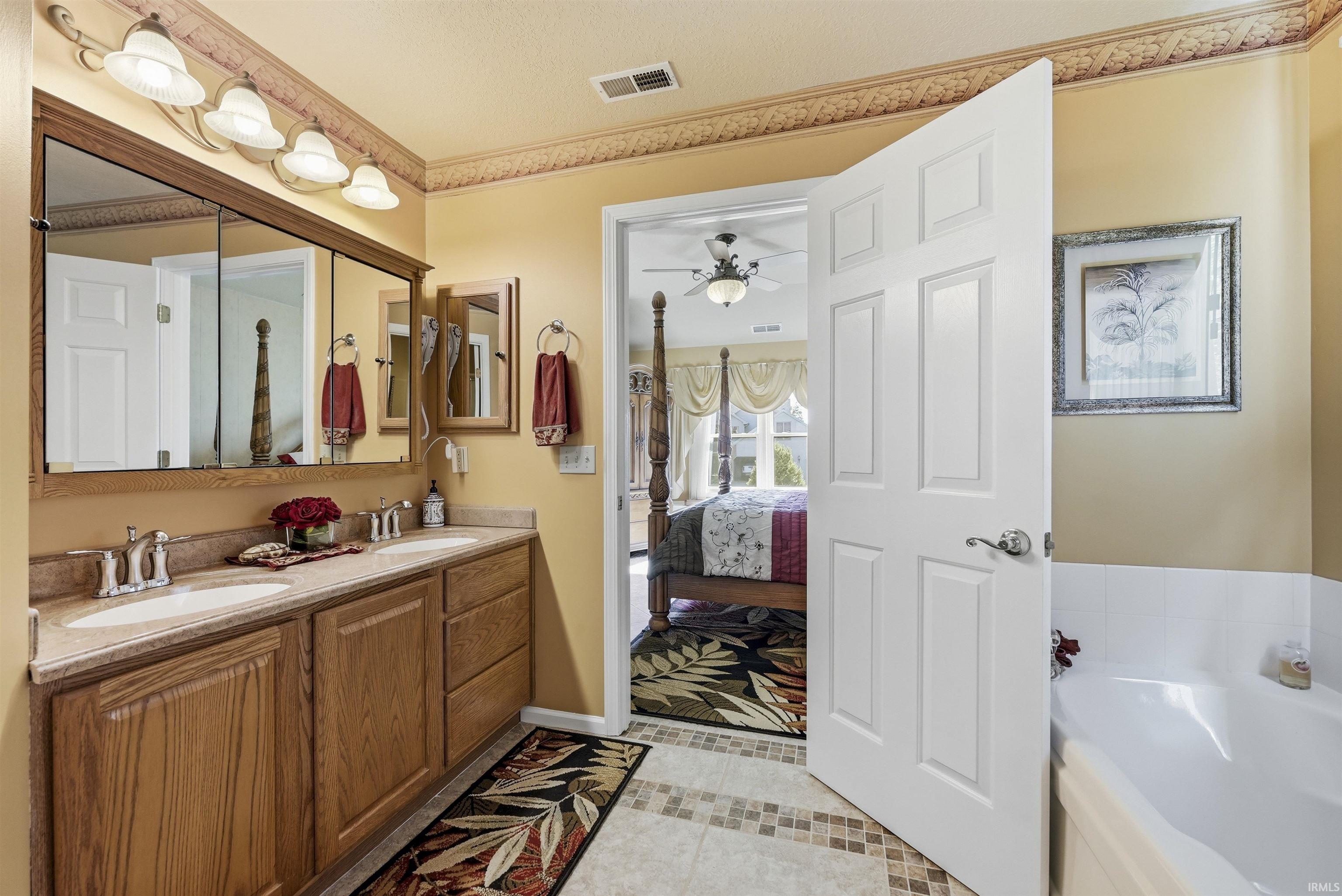 Spa-inspired primary bathroom featuring a wood-finish vanity with dual sinks, polished countertop, and illuminated mirror