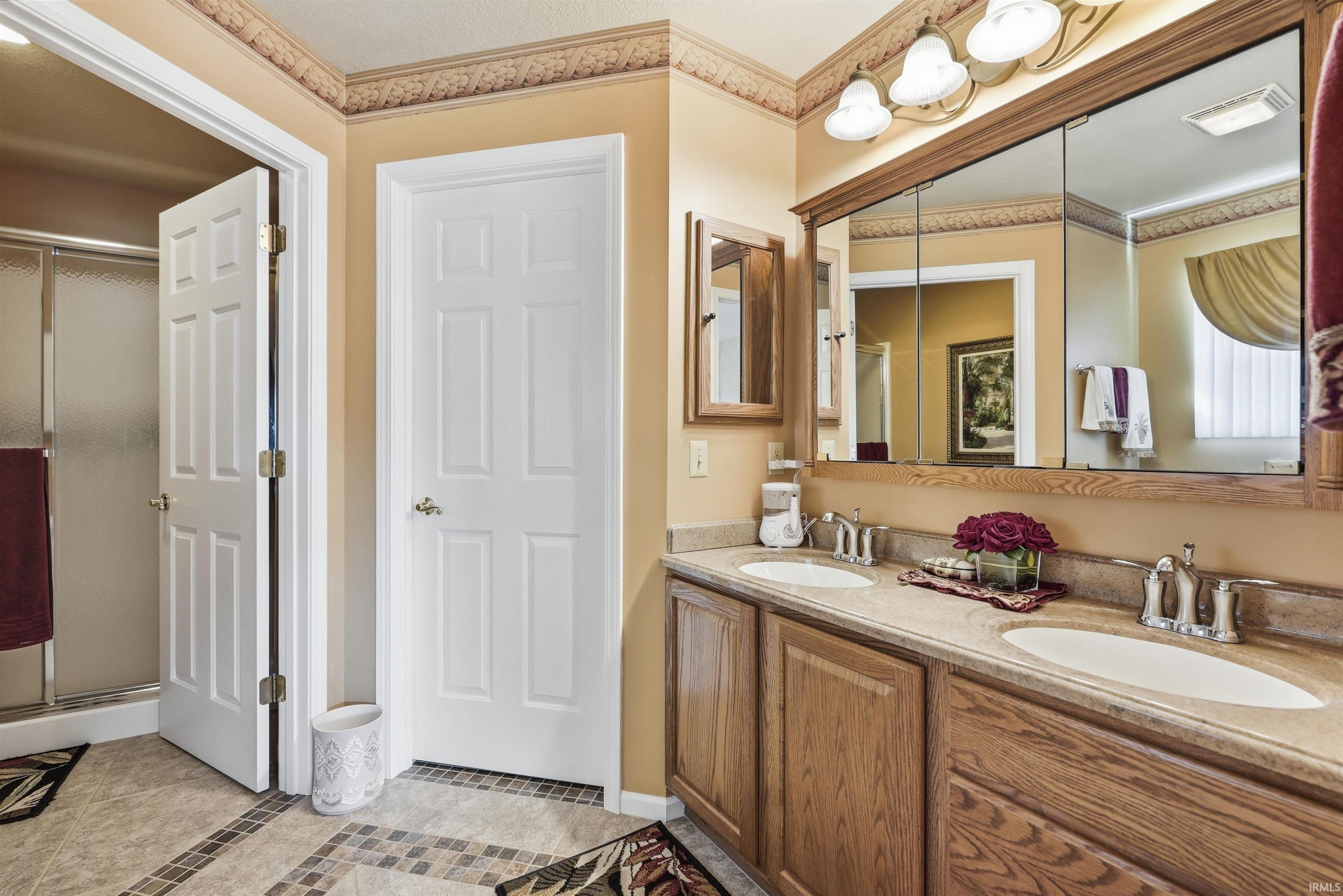 Bathroom featuring a dual-sink vanity with wood cabinetry, a large medicine cabinet mirror, and individual chrome faucets