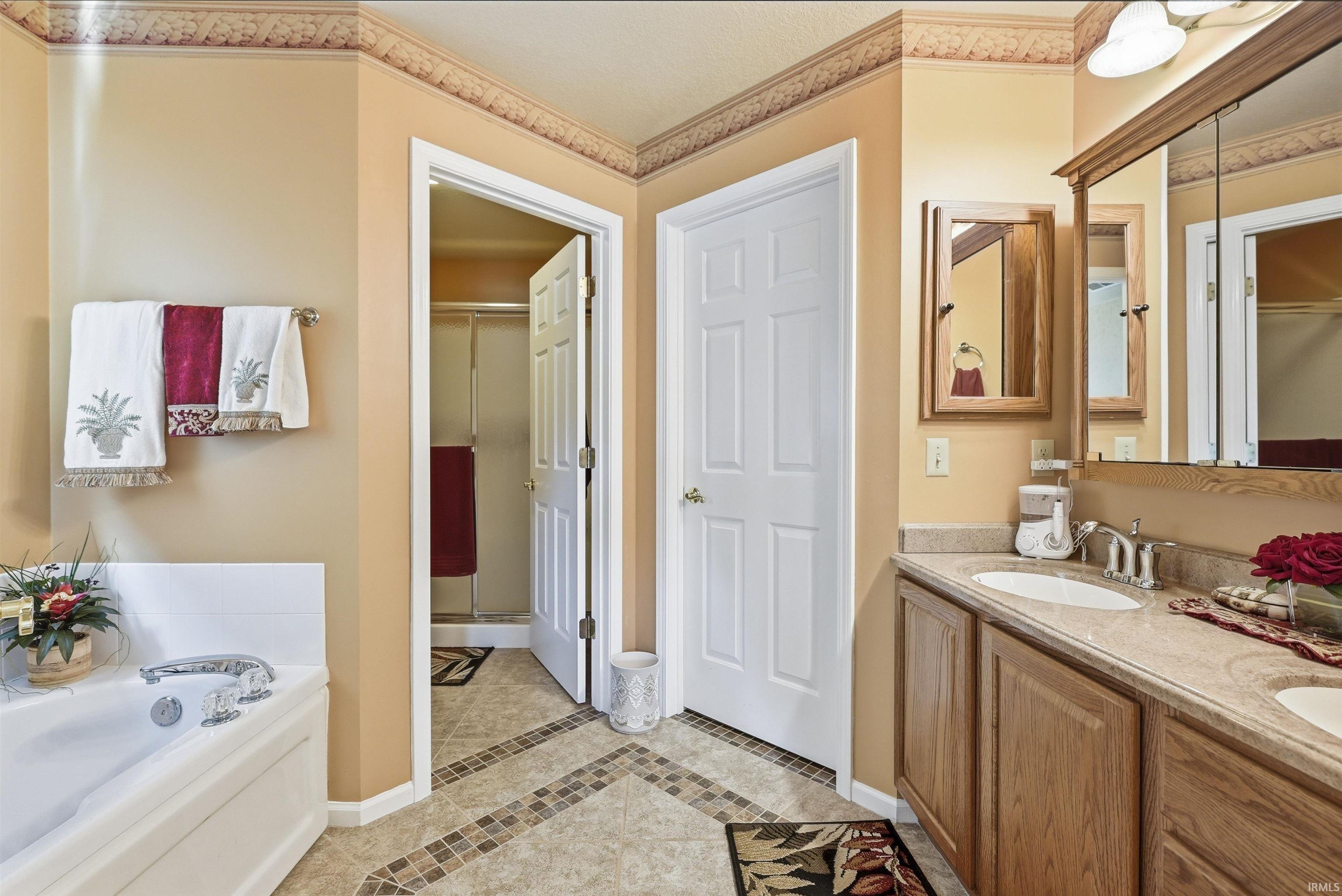 Spa-inspired master bath featuring a soaking tub with deck surround, dual-sink vanity with wood cabinetry and granite countertops, large framed mirror, and tile flooring