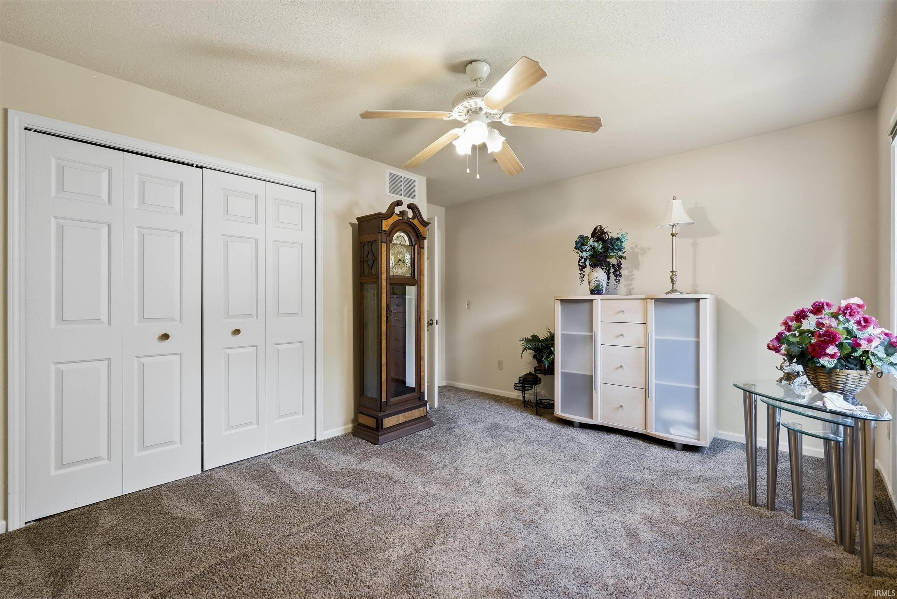 Spacious primary bedroom featuring plush carpeting, a ceiling fan with integrated lighting, and triple-panel white closet doors providing ample storage