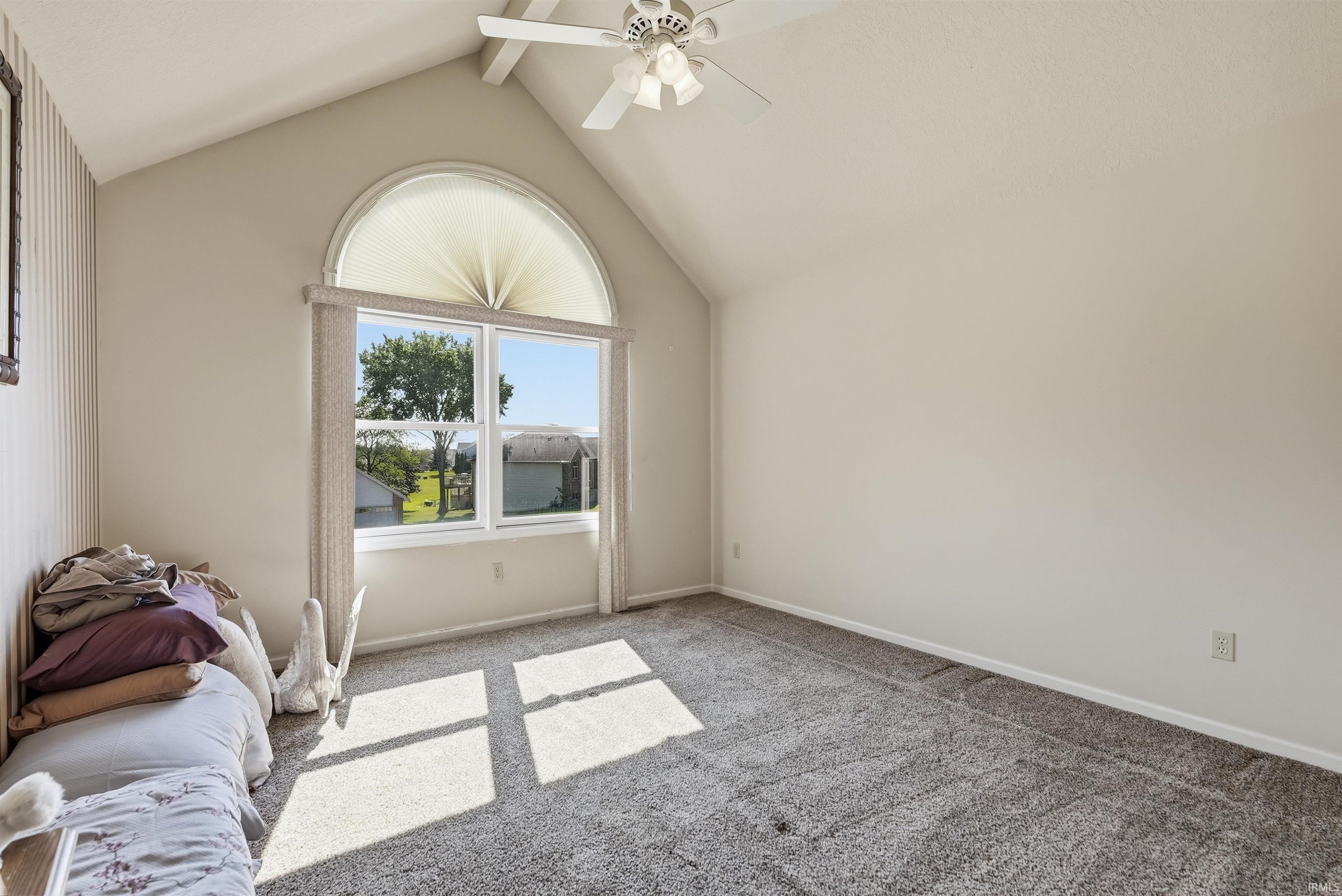 Bright and airy bedroom showcasing vaulted ceilings, an arched glass door with transom window flooding the space with natural light, ceiling fan with integrated lighting, and neutral wall finishes