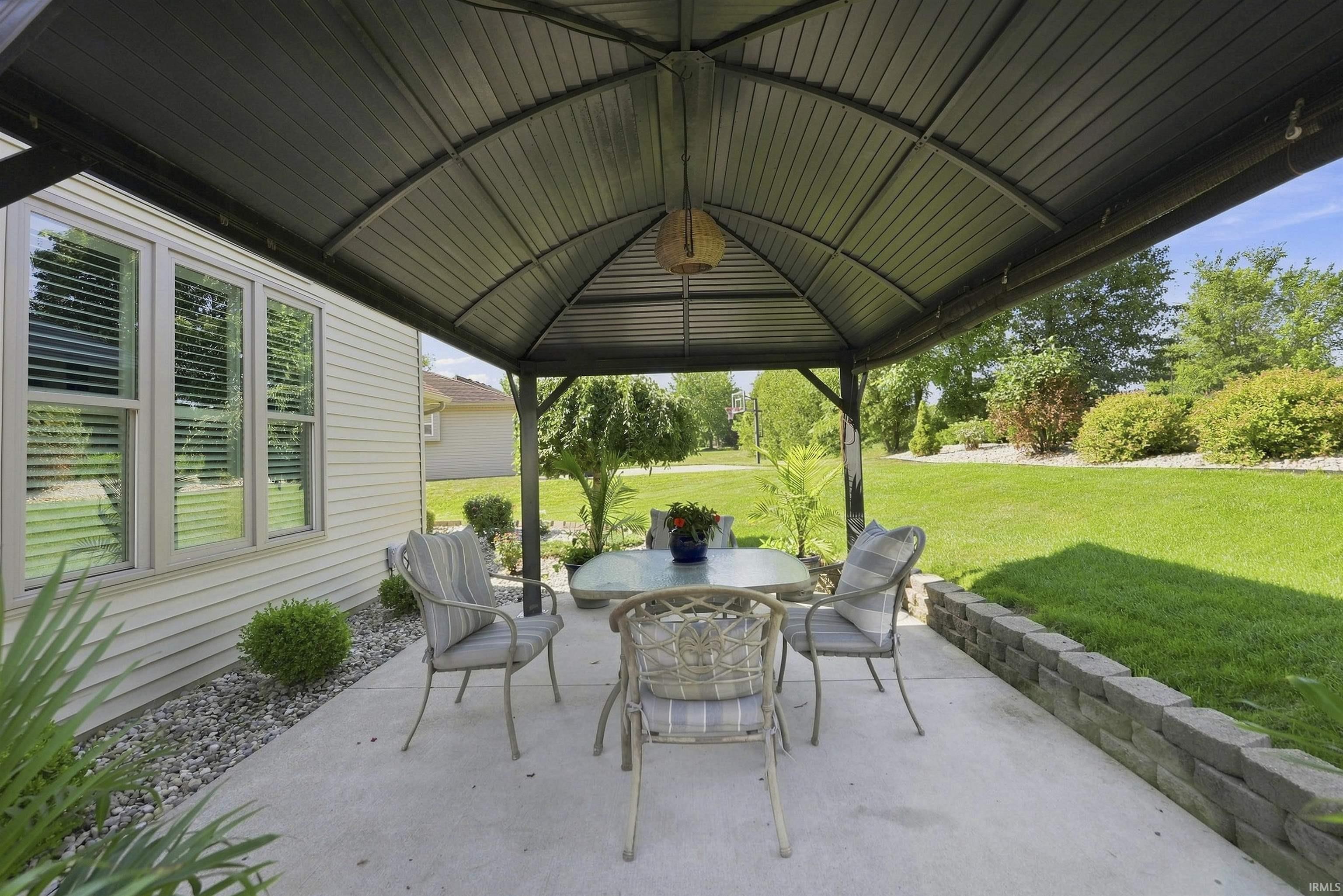 Covered patio with arched metal roof and concrete flooring, furnished with four chairs and a round table