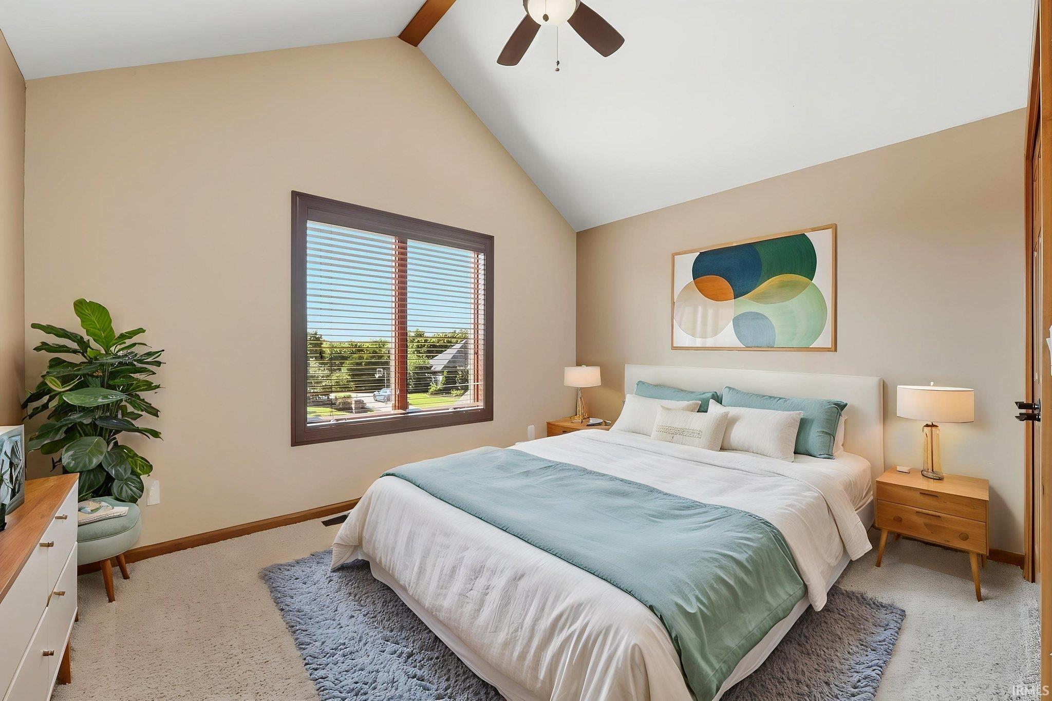 Bright primary bedroom featuring vaulted ceilings with exposed wood beams, large dual-pane windows with plantation shutters, and soft neutral wall finishes