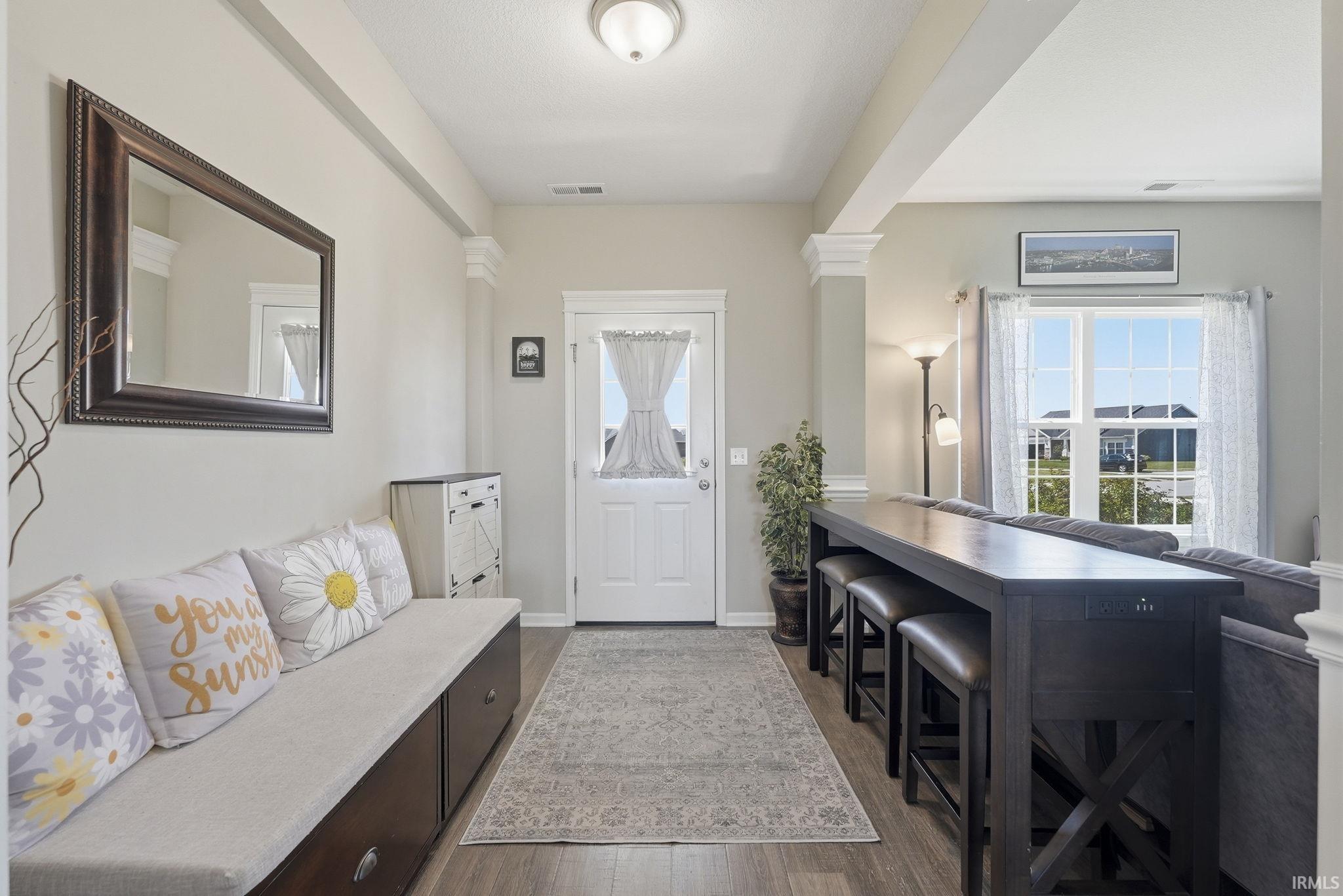 Welcoming foyer featuring a coffered ceiling, large framed mirror, and abundant natural light from dual glass doors and windows