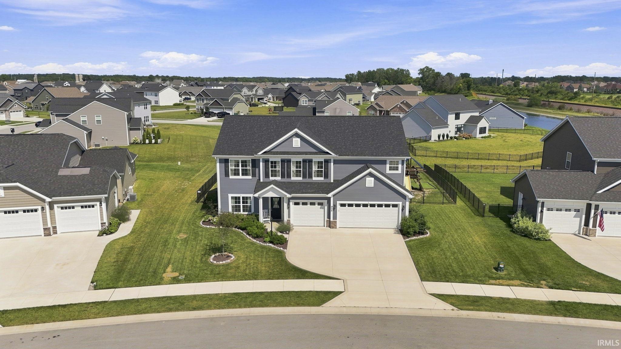 Charming two-story colonial with gray fiber cement siding and white trim, featuring a three-car attached garage, curved driveway, and professionally manicured lawn with mature landscaping