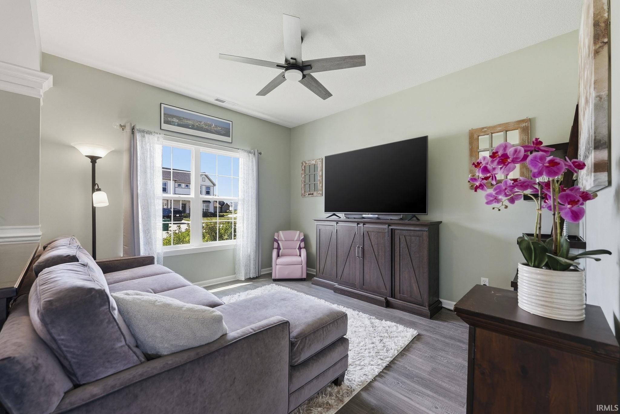 Spacious living area featuring wood-finish flooring, light-toned walls, crown molding, a ceiling fan, and a large window