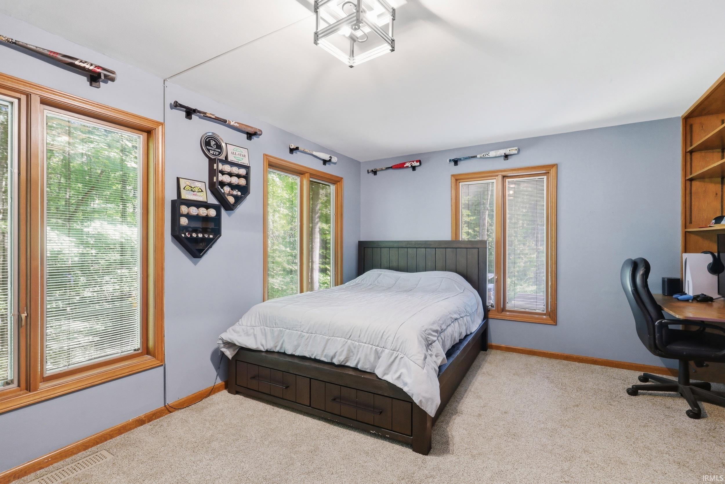 Bedroom featuring wood-trim windows, light-colored carpeting, a ceiling-mounted light fixture, and built-in wood shelving