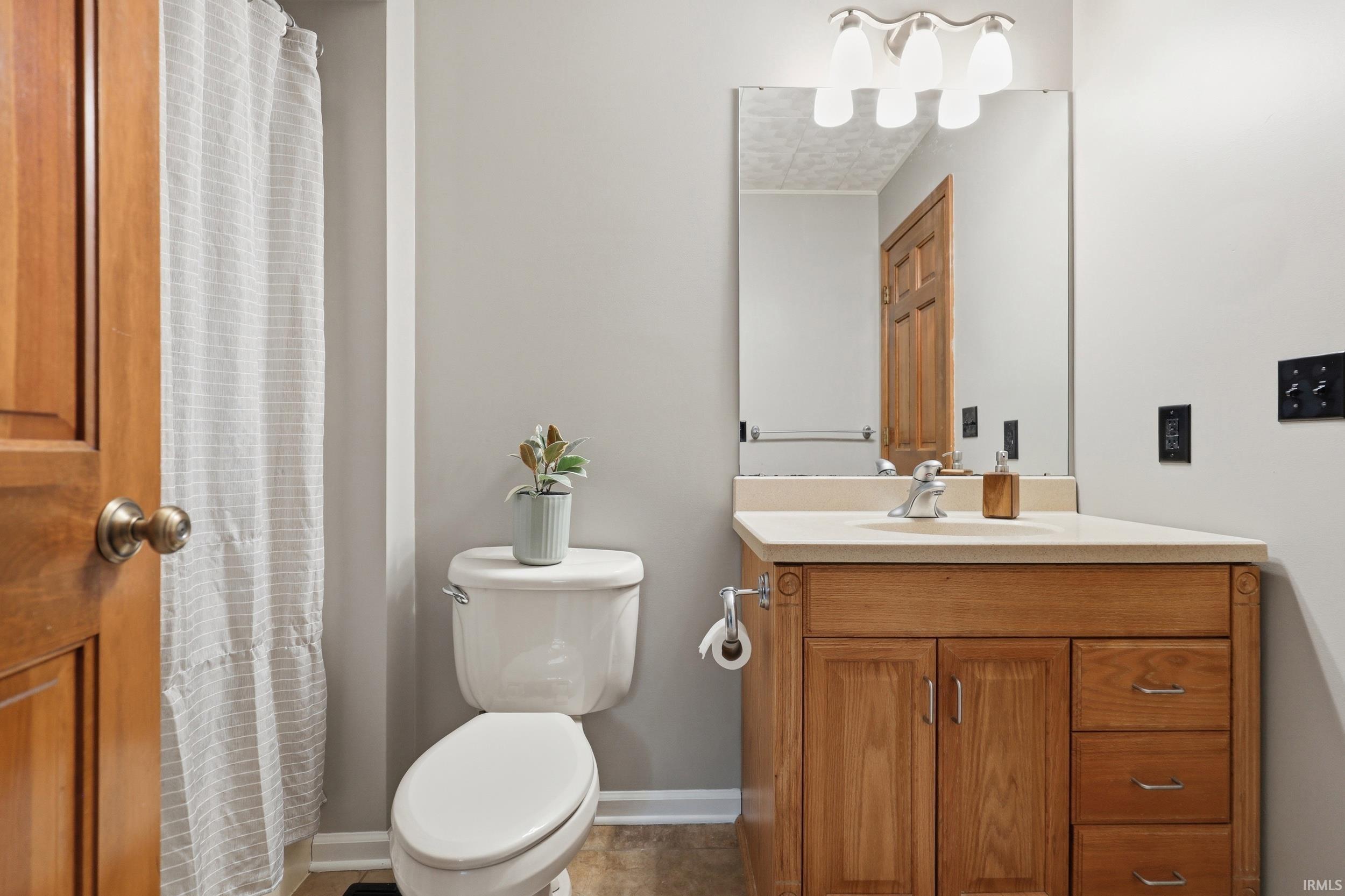 Bathroom featuring a light wood-finish vanity with a light countertop, a rectangular mirror, and a three-light vanity fixture