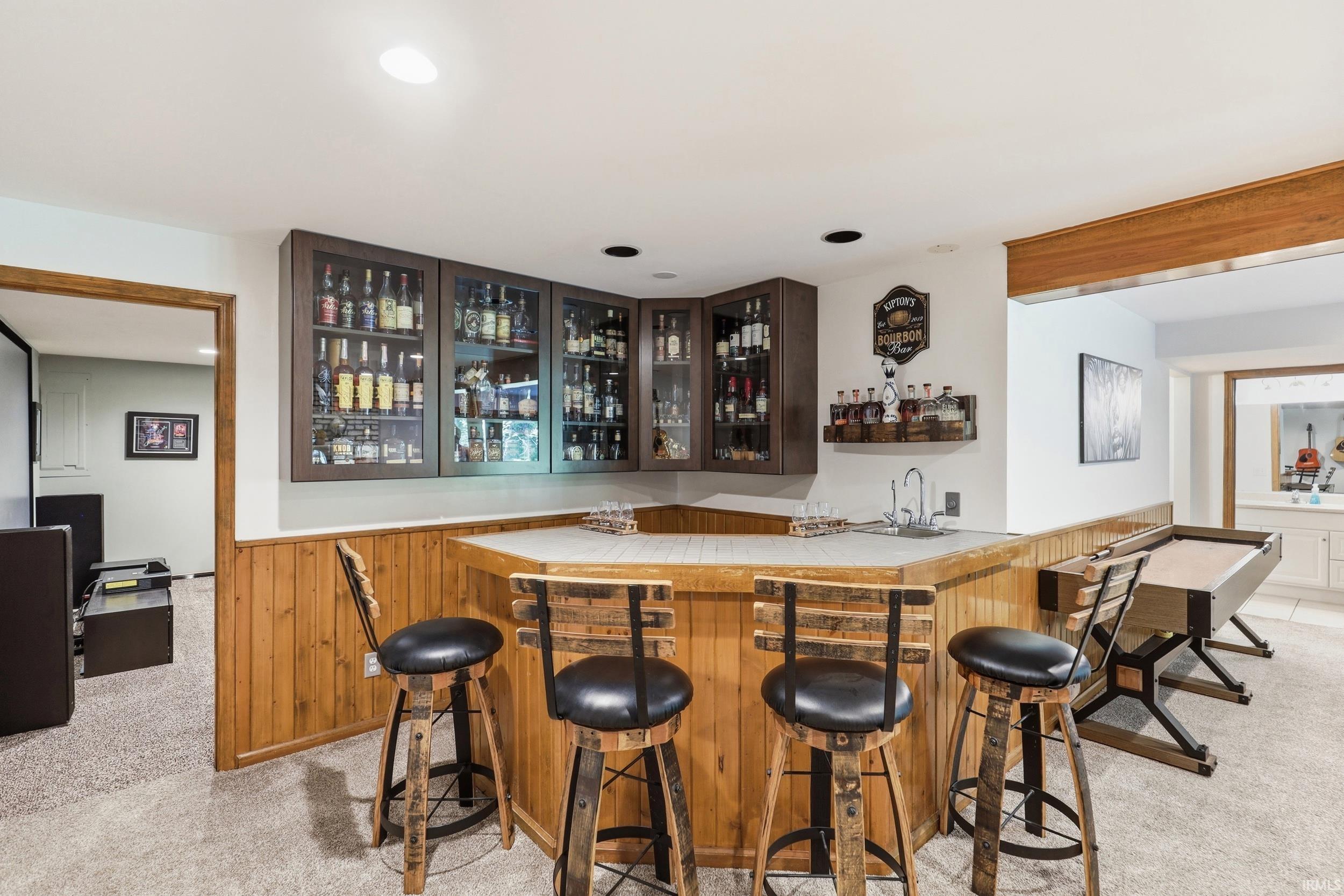 Built-in wet bar featuring upper glass-front cabinetry, a light-toned countertop, and wood-paneled base