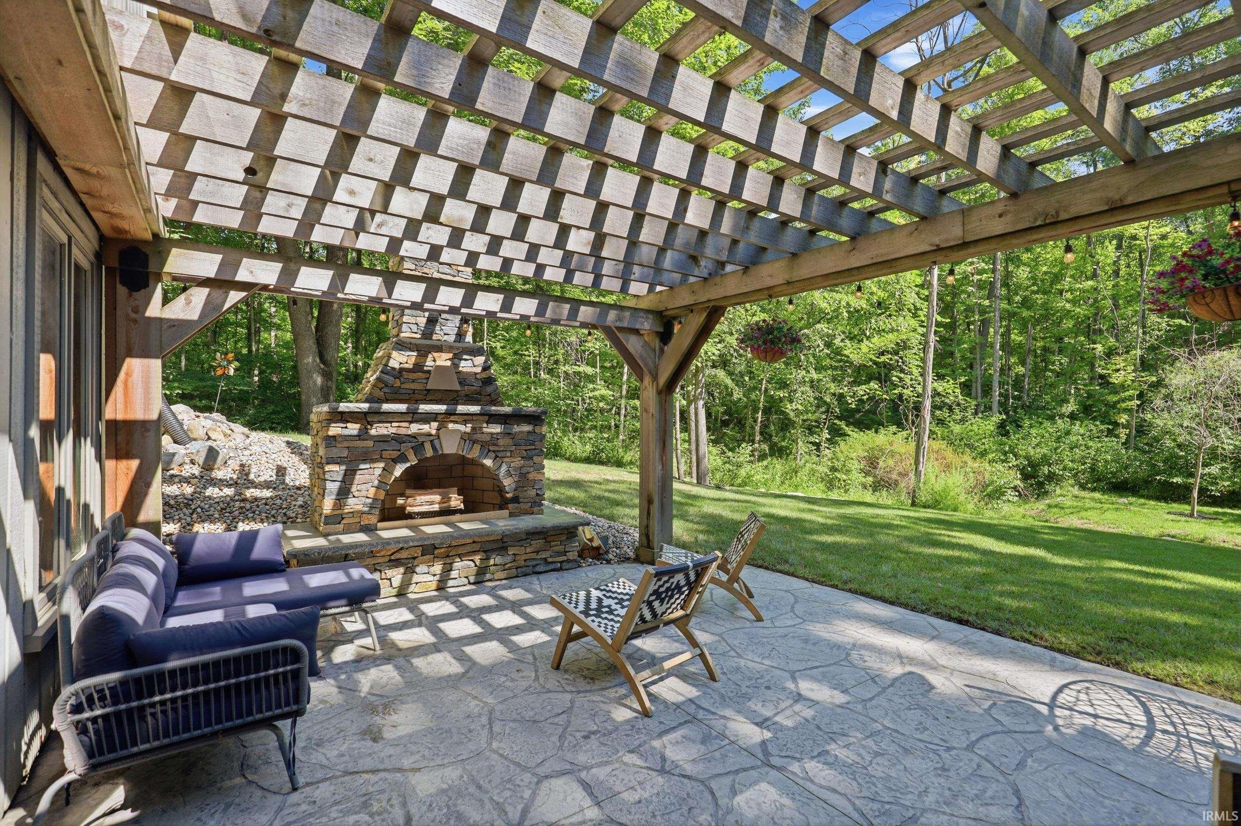 Outdoor living space featuring a wood pergola, stamped concrete patio, and stone-clad fireplace