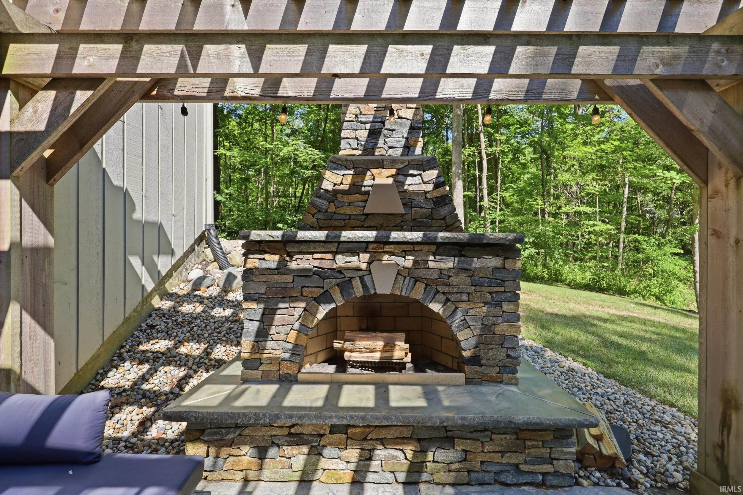 Outdoor stone-clad fireplace with arched firebox under a pergola structure