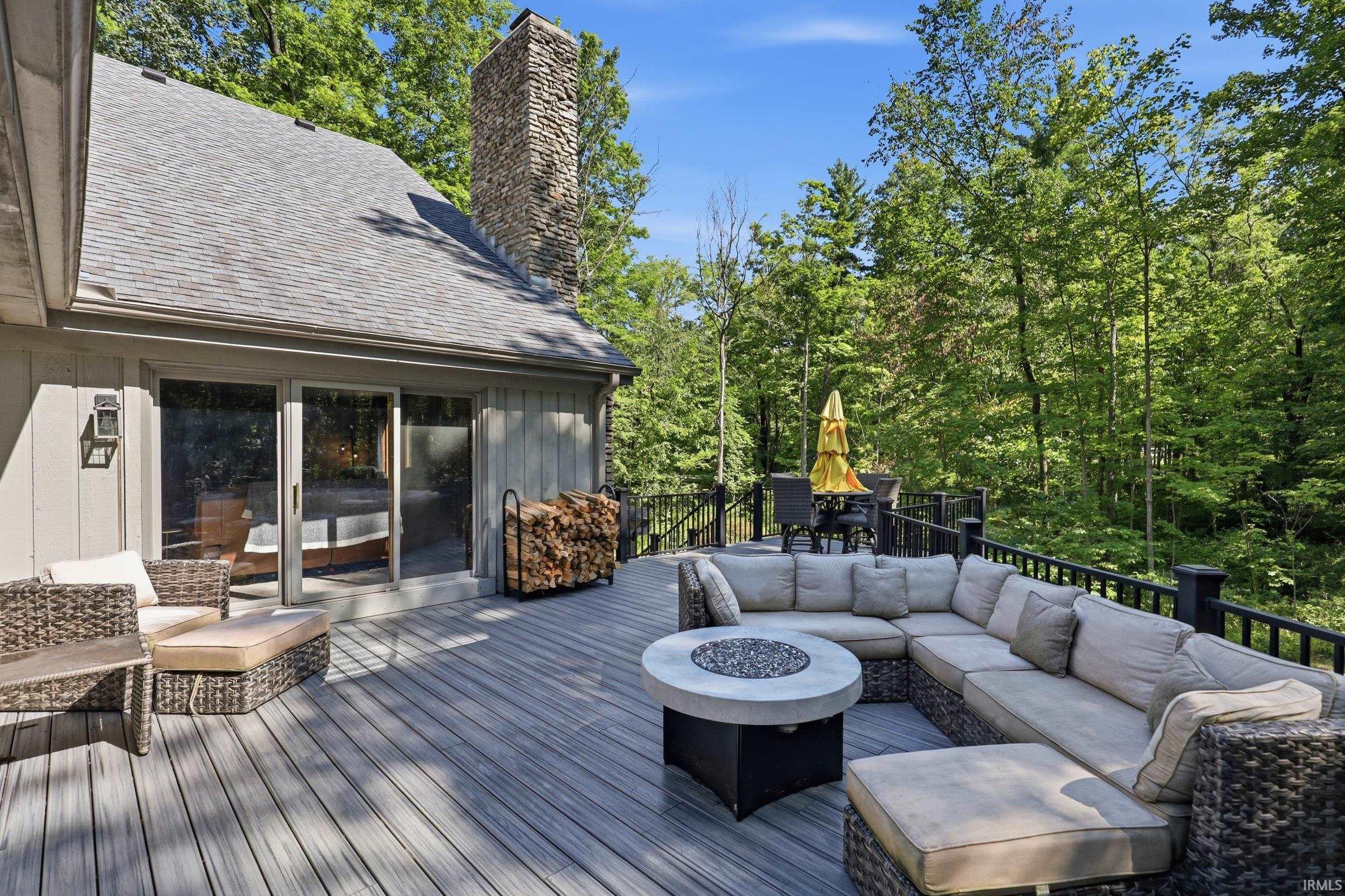 Expansive outdoor deck featuring wood-finish composite decking, a stone-clad chimney, sliding glass doors, and a black metal railing