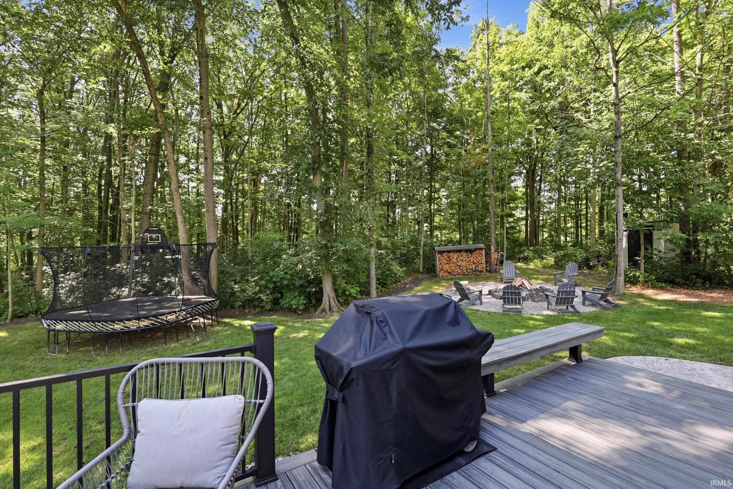 Expansive backyard featuring a composite deck, stone fire pit area with seating, and mature tree-lined perimeter