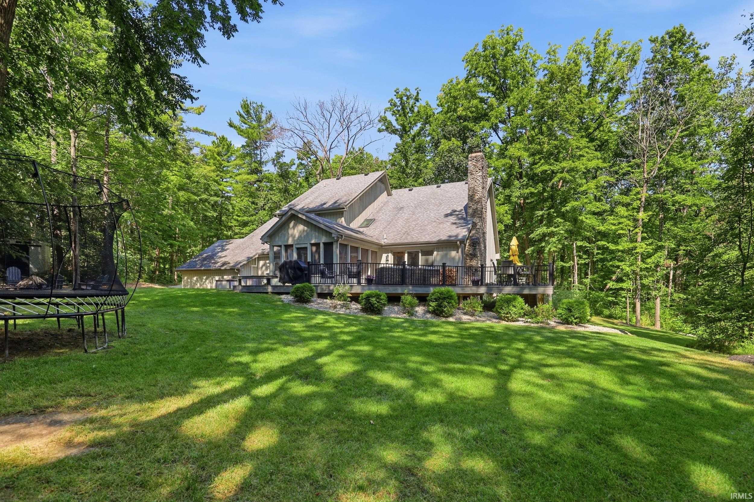 Rear elevation featuring an expansive lawn, a stone chimney, a spacious deck, and a screened porch