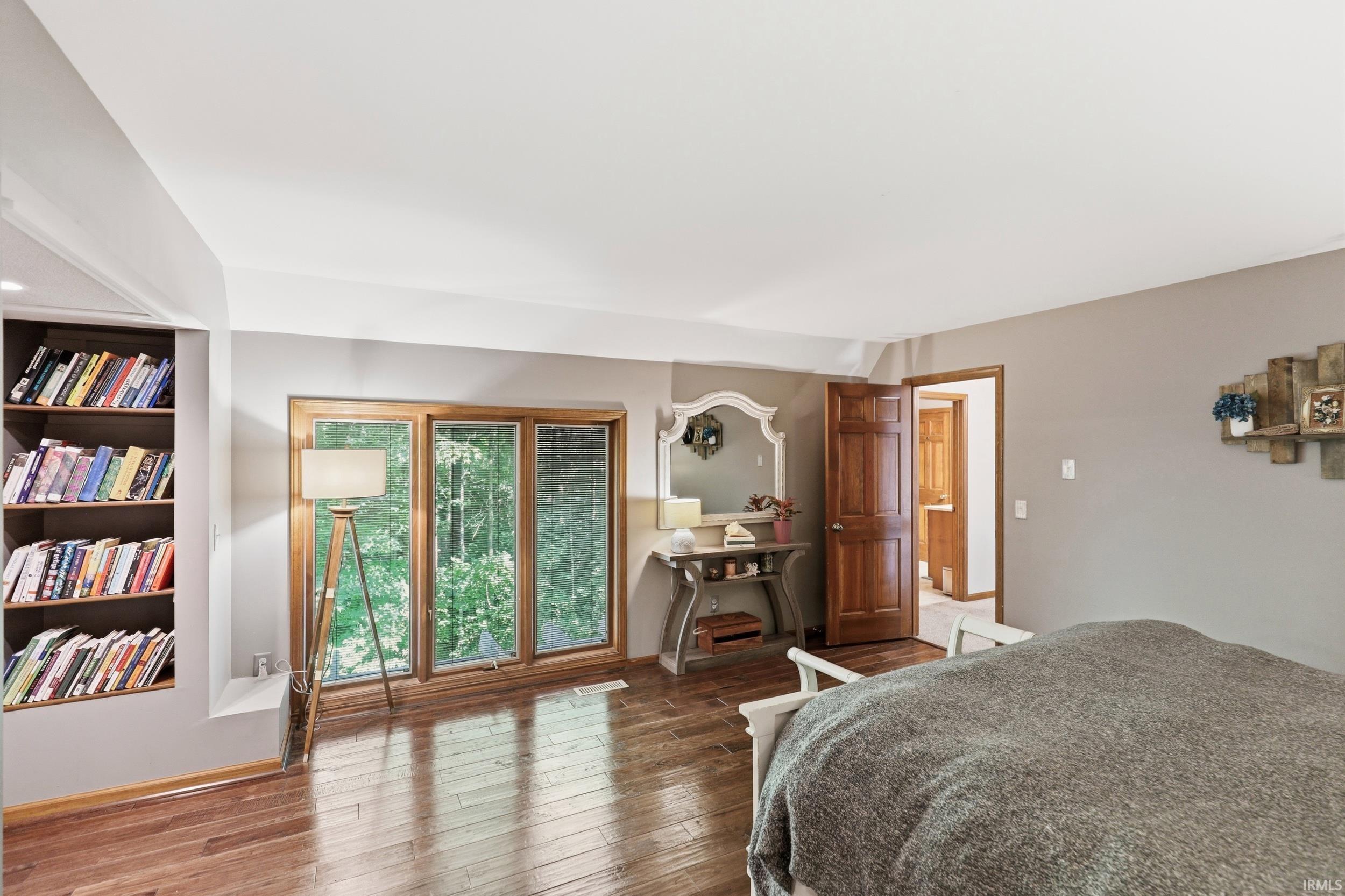 Hardwood-finish flooring throughout, featuring a built-in bookshelf, large windows, and a solid wood door