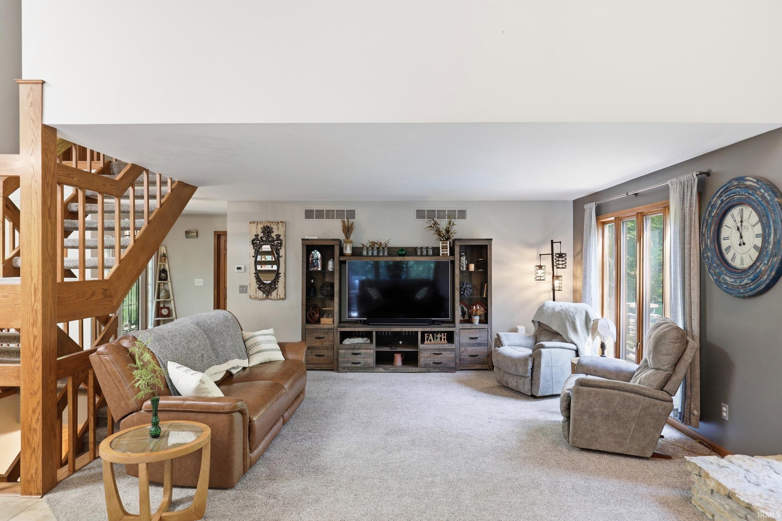 Carpeted living space featuring substantial wood staircase, large wood-framed glass doors, and a built-in media console