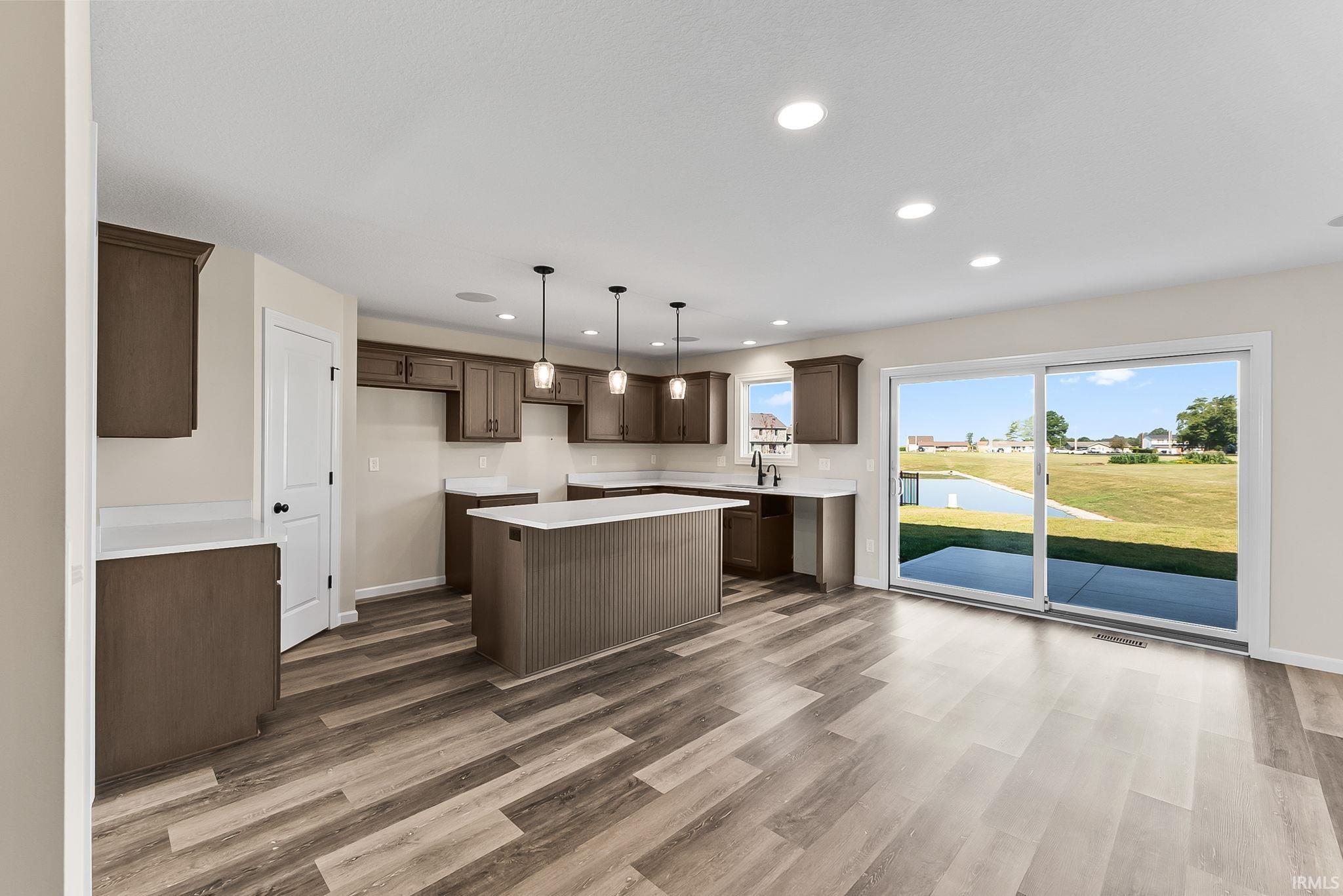 Open-concept kitchen and dining area featuring rich wood-finish cabinetry, a large island with seating, stainless steel appliances, and pendant lighting