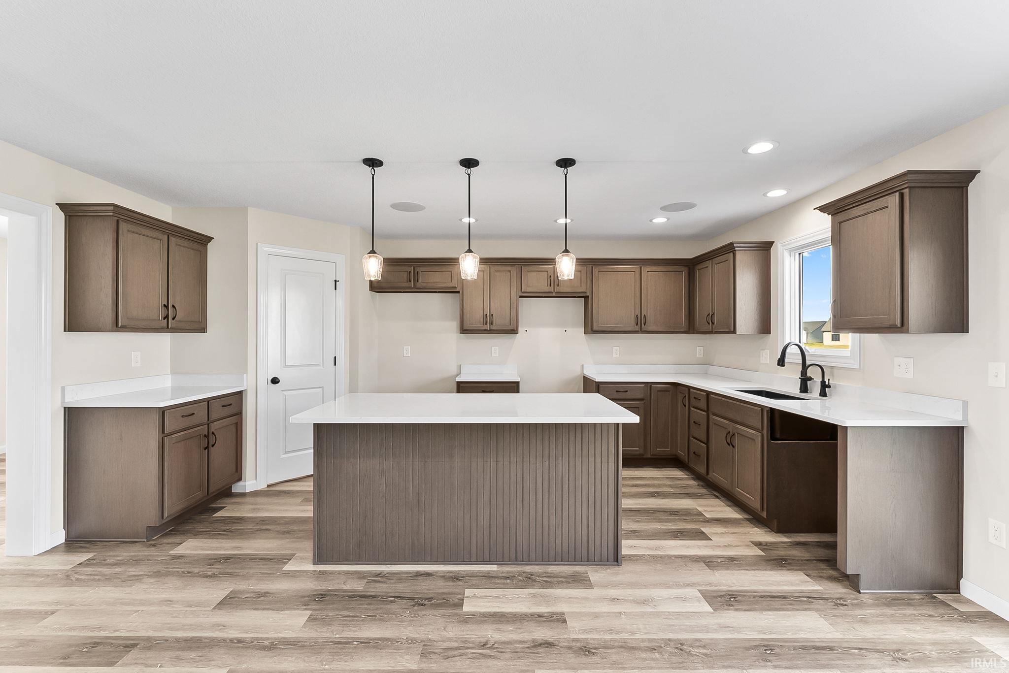 Open-concept kitchen featuring an island with pendant lighting, ample cabinetry, white countertops, wood-finish flooring, and a black sink with a matching faucet