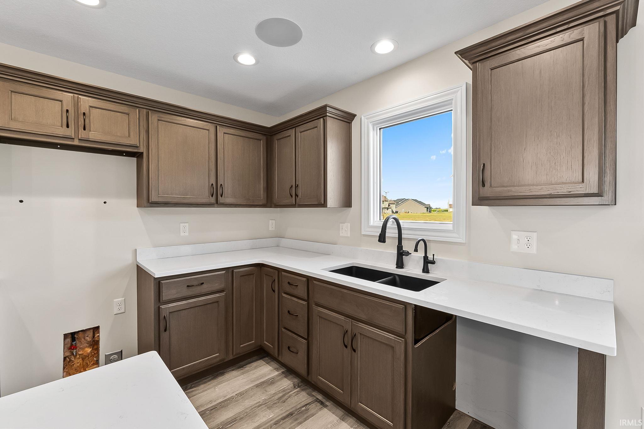 Modern laundry room featuring rich wood-finish cabinetry with ample storage, white quartz countertops, a stainless steel sink with matte black faucet, and engineered wood flooring