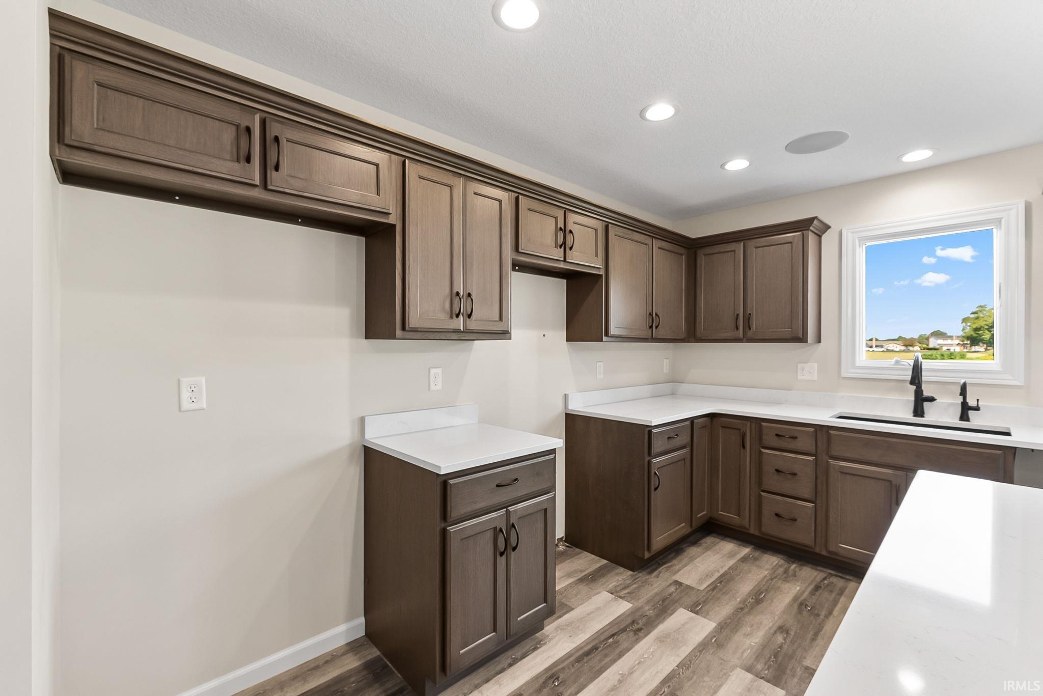 Kitchen featuring rich wood-finish cabinetry, white countertops, wood-finish flooring, recessed lighting, and a window with a black faucet