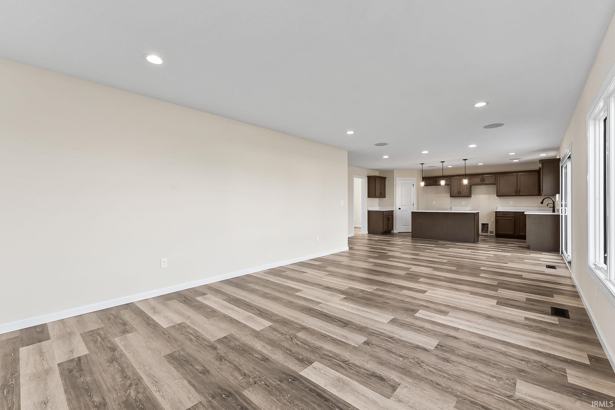 Open-concept living space featuring extensive wood-finish plank flooring, recessed ceiling lighting, and a seamlessly integrated kitchen with dark cabinetry, stainless steel appliances, and a centered island