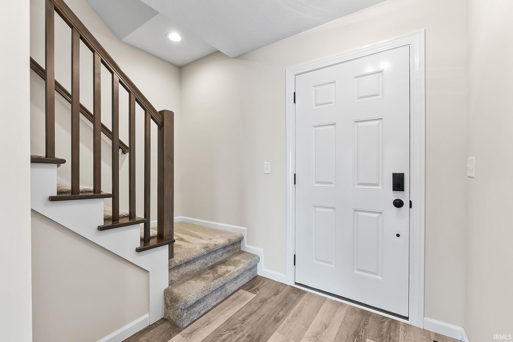 Welcoming foyer featuring a wood-finish staircase with dark metal railings, recessed ceiling lighting, and a six-panel white entry door with sidelights