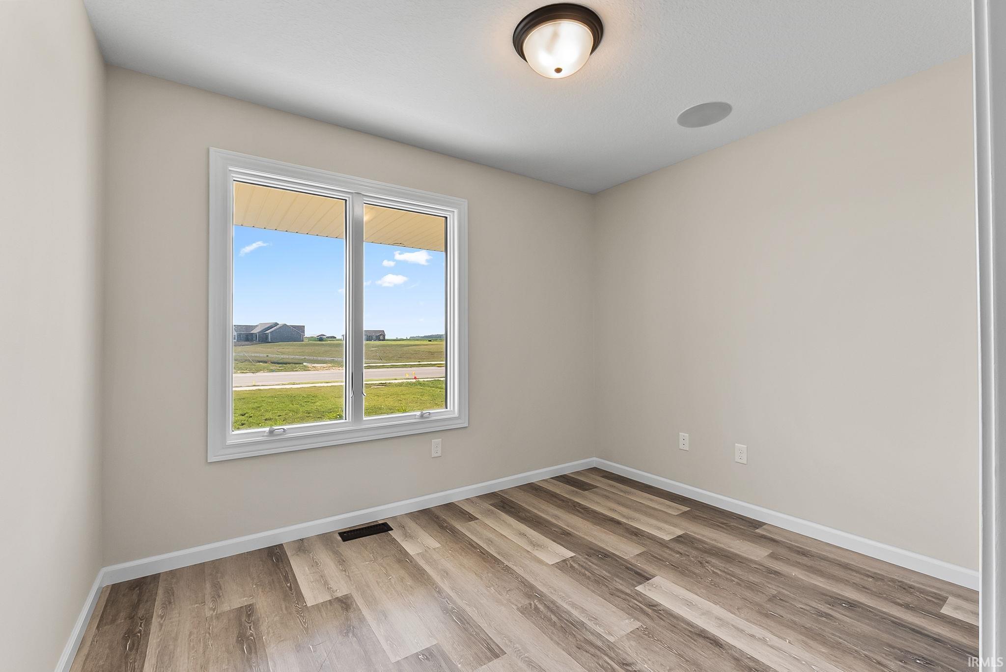 Neutral-toned room featuring a large window, wood-finish flooring, white baseboards, and a ceiling-mounted light fixture